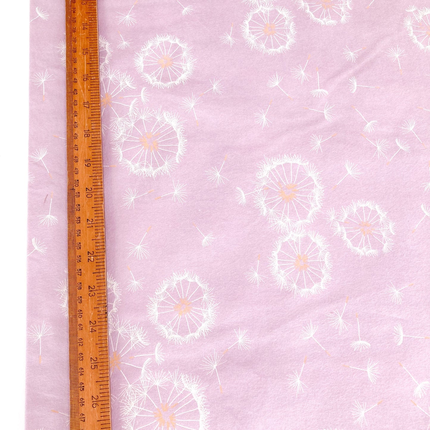 Lilac brushed cotton fabric with dandelion pattern and a wooden ruler for scale.