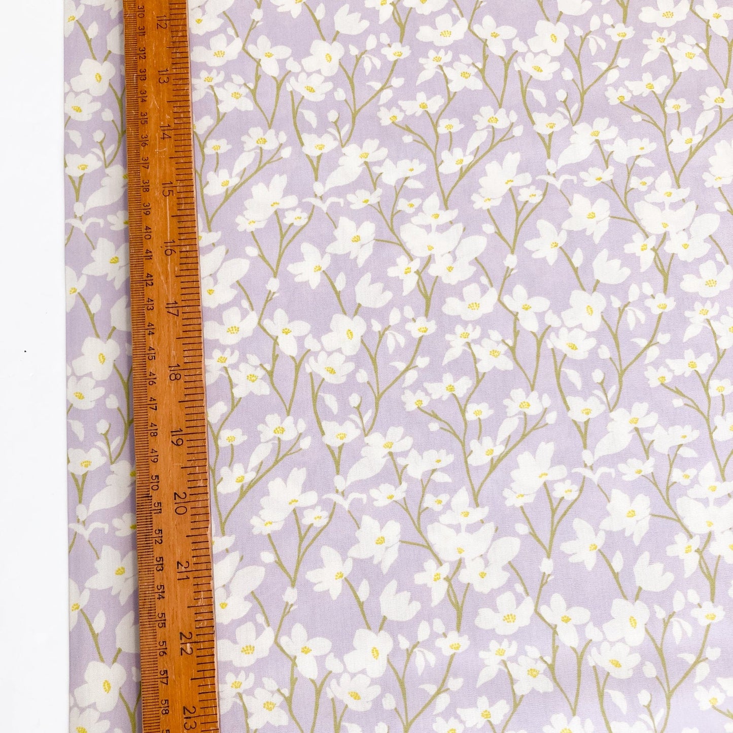 Floral cotton fabric with cream flowers on a lilac background with a ruler for scale