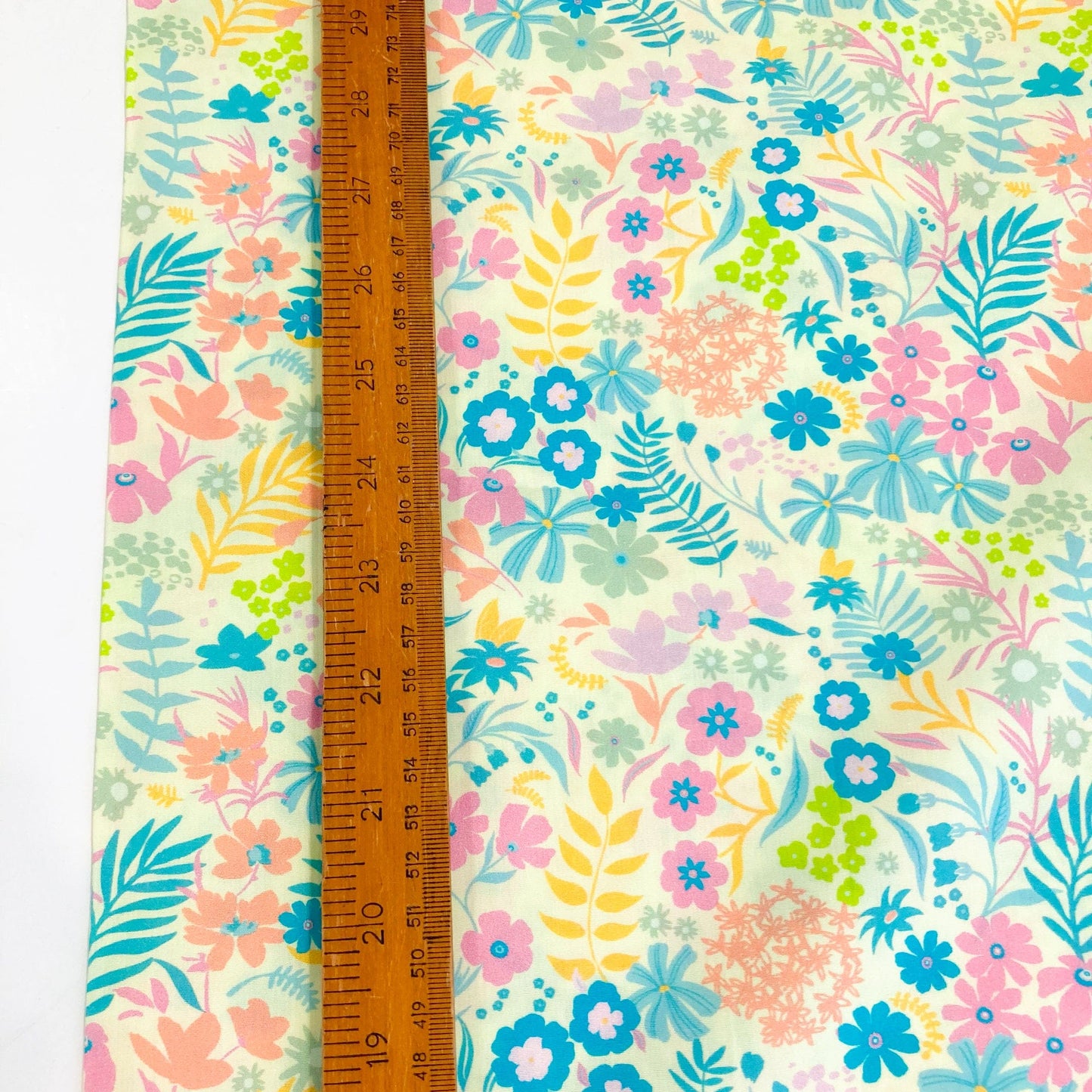 Floral quilting cotton by Art Gallery Fabrics with pink, blue, green, and yellow flowers on a yellow background against a ruler for scale.