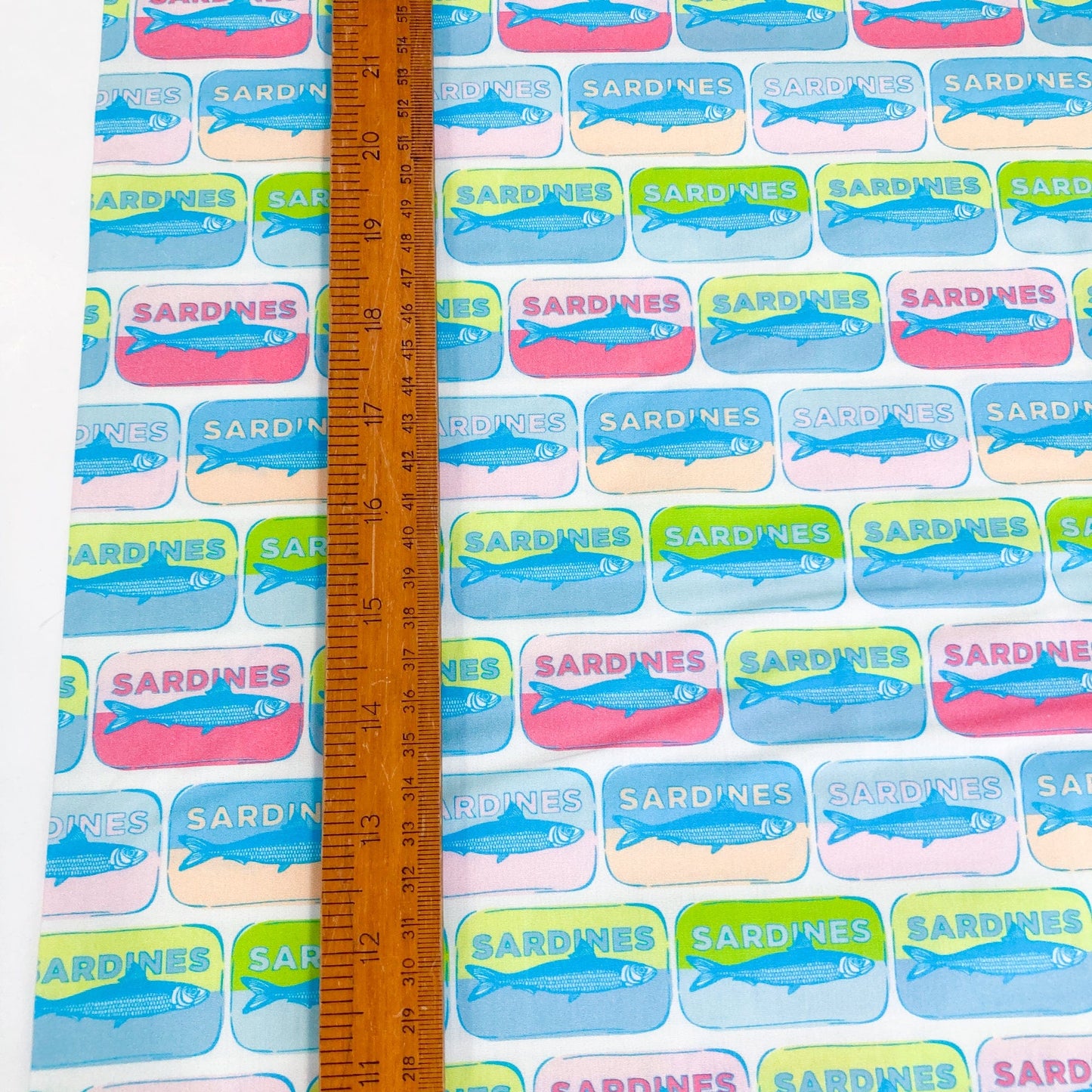 Quilting cotton with colorful pop-art style sardine tin pattern with a ruler for scale.