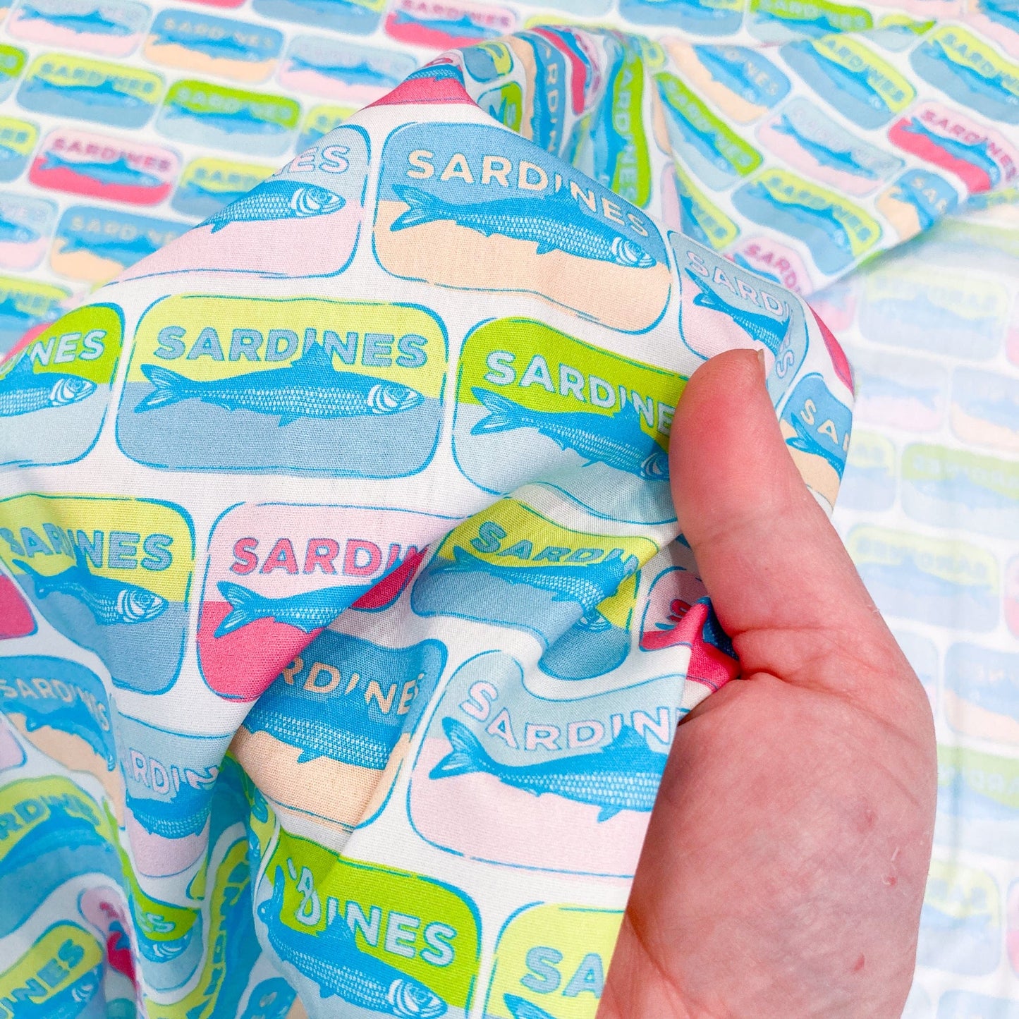 Quilting cotton with colorful pop-art style sardine tin pattern held against a hand for scale.