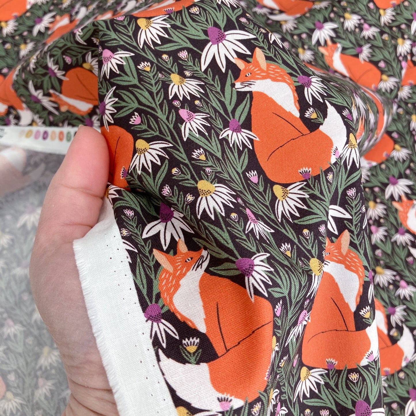 Organic quilting cotton with fox and floral pattern. held by a hand