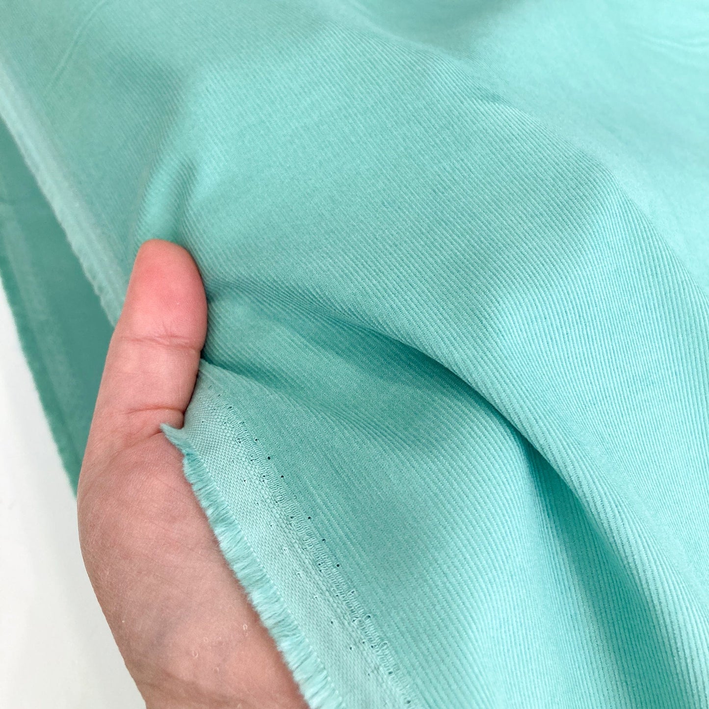 Close-up of turquoise cotton needlecord fabric with a hand holding it