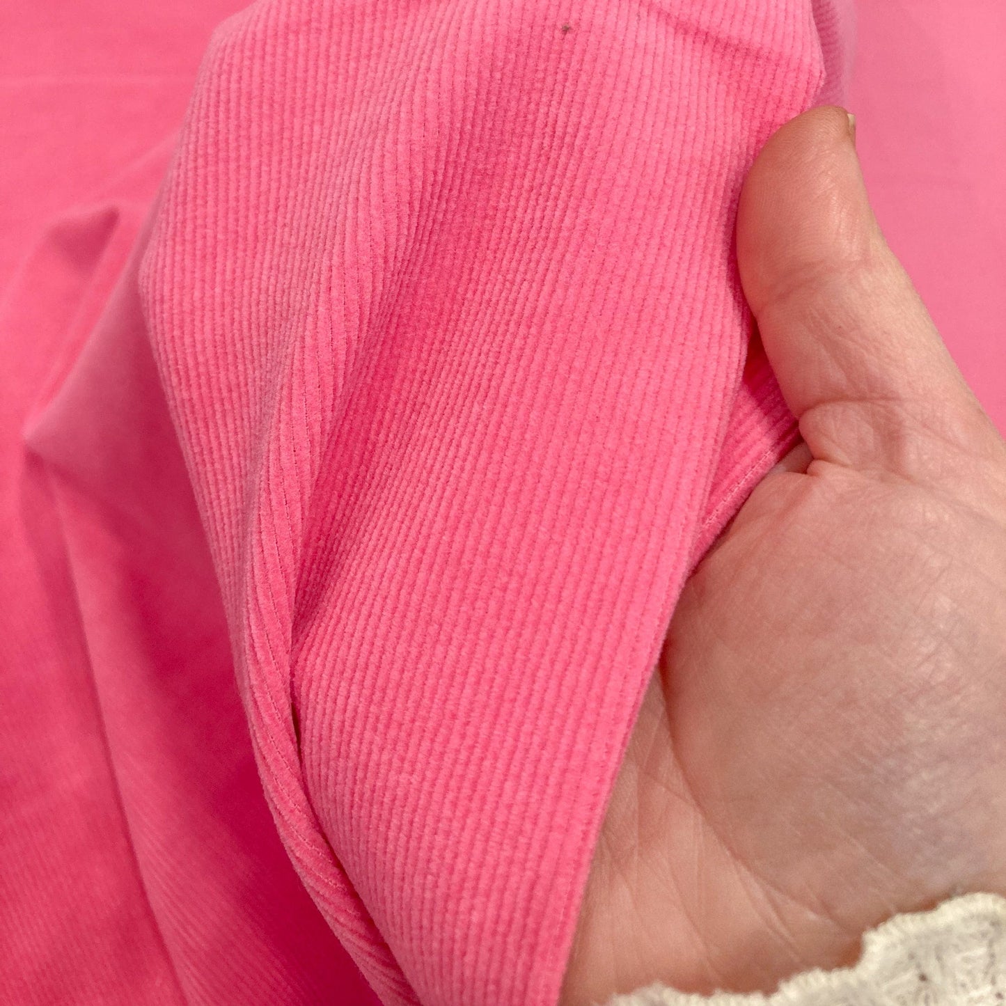 Close-up of a hand holding bright pink cotton corduroy fabric