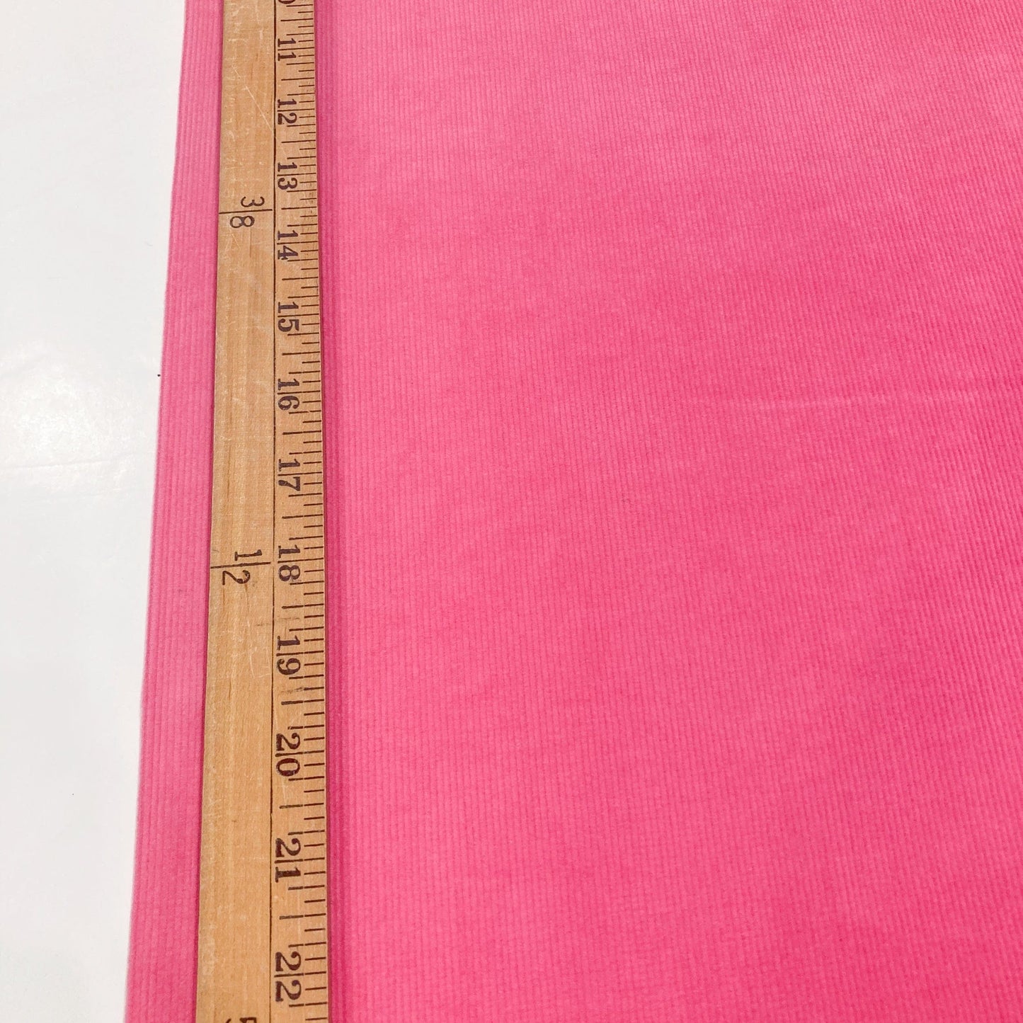 Bright pink cotton corduroy fabricwith a wooden measuring ruler for scale