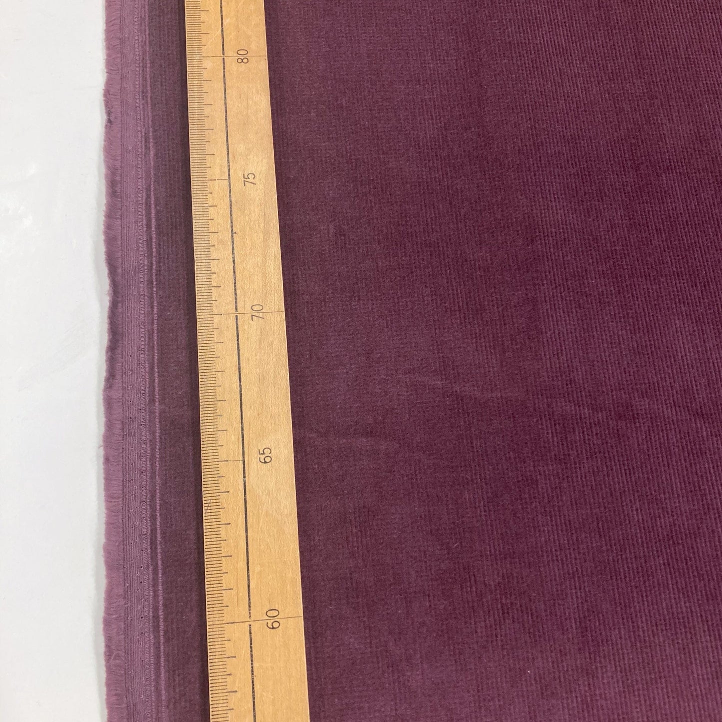 Purple corduroy fabric with a wooden ruler for scale on a white background