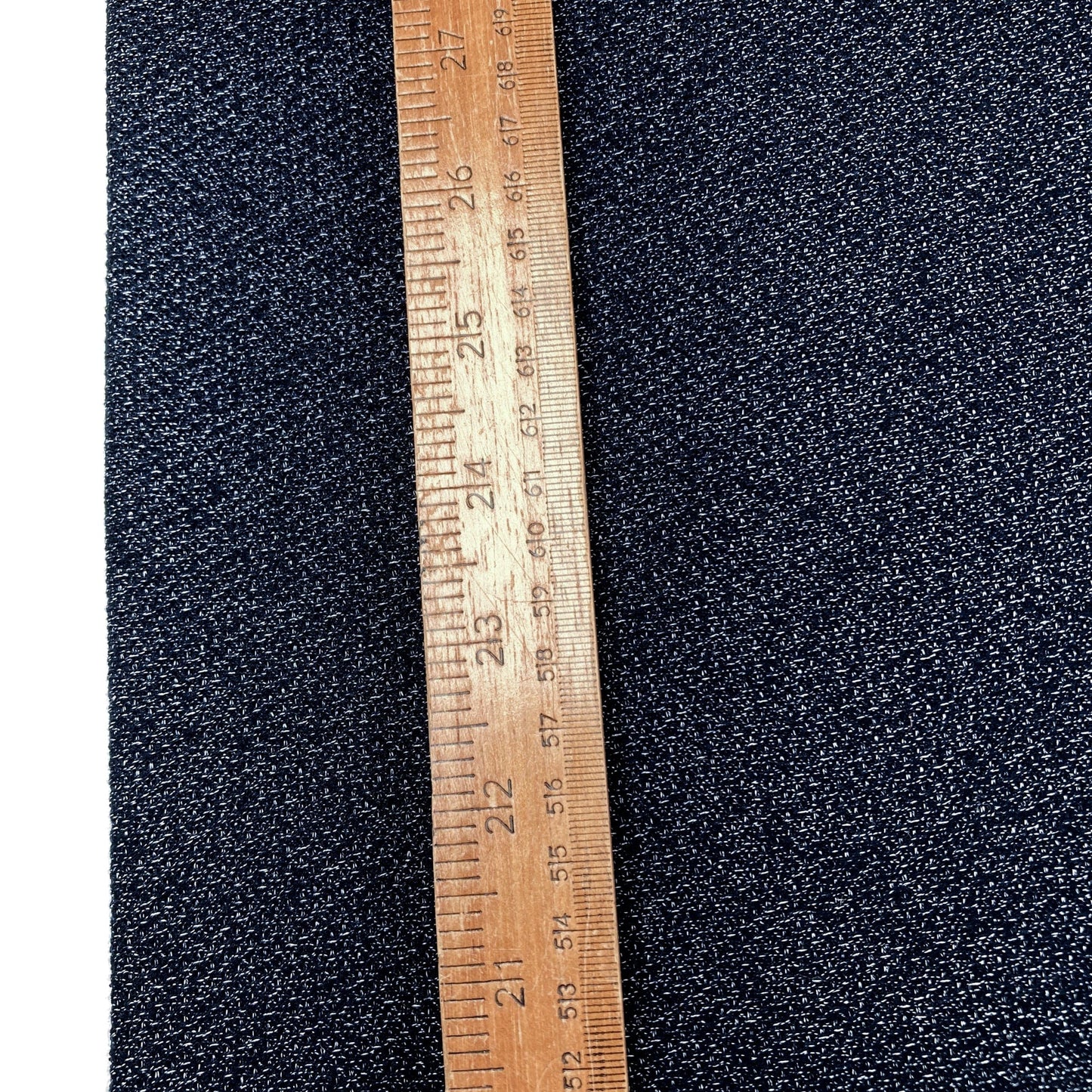 Textured dark blue fabric with a wooden ruler for scale on a white background