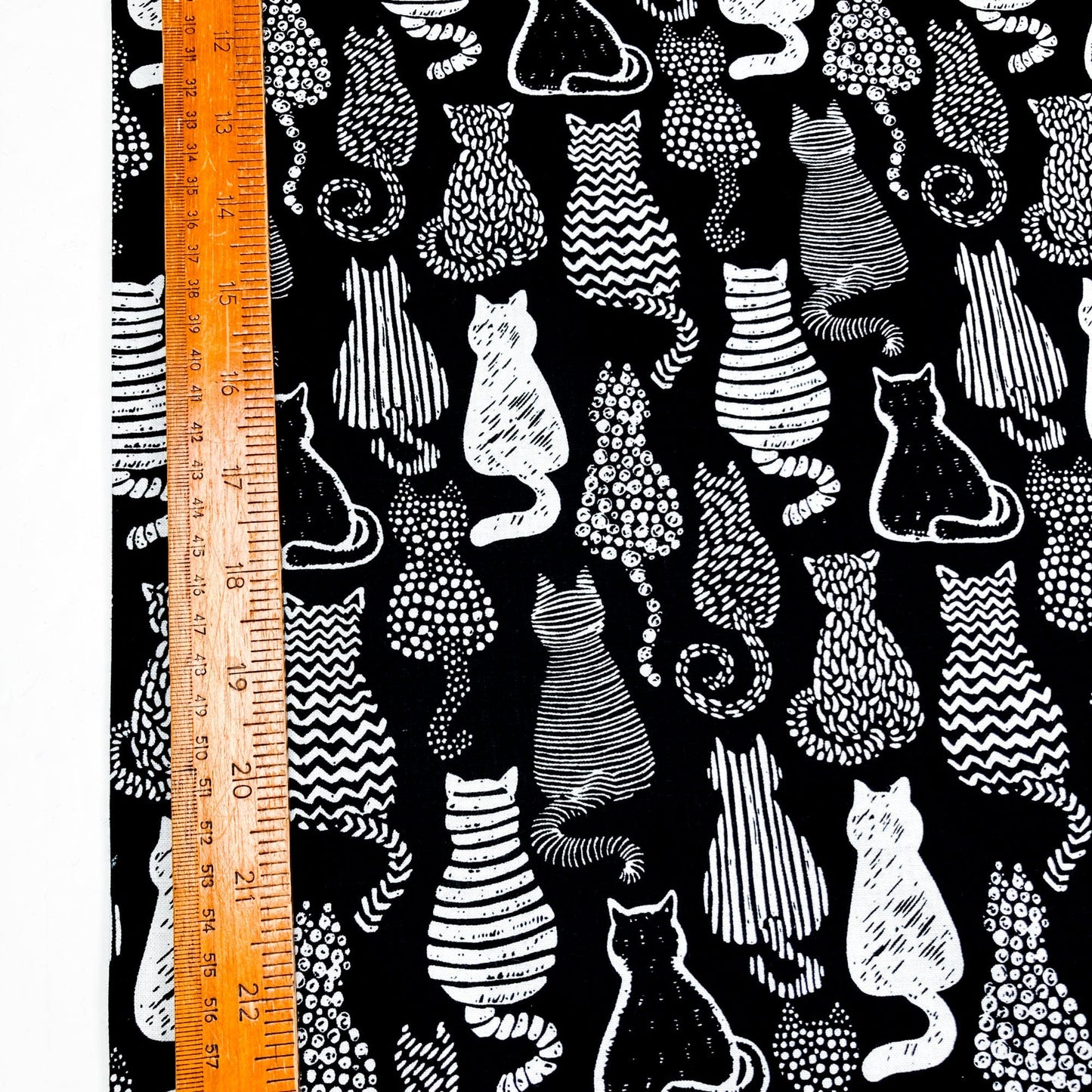 Cotton fabric with a graphic style cat print in black and white shown against a ruler for scale.