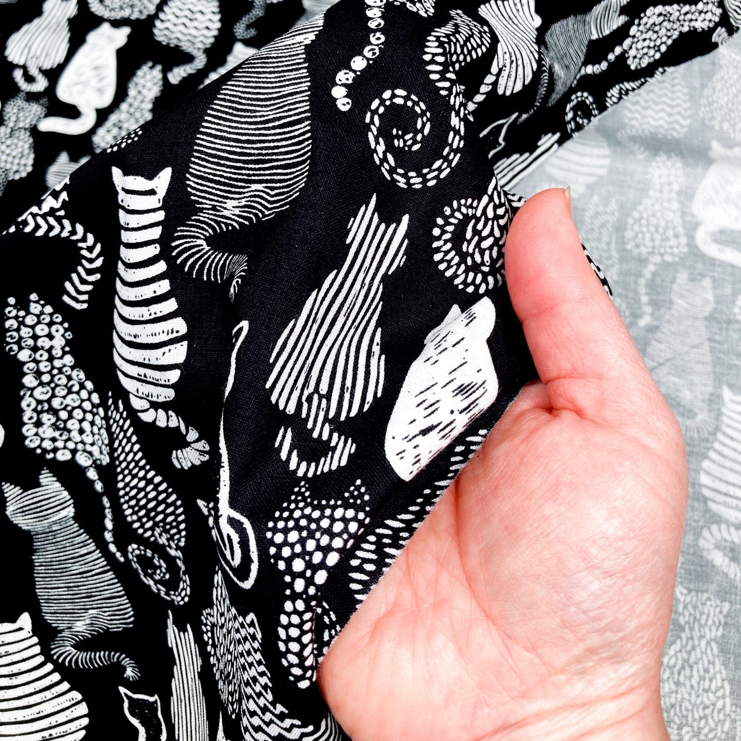 Cotton Fabric with a graphic style cat print in black and white held in a hand.