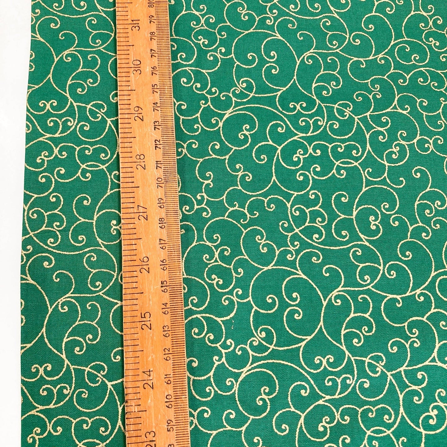 Green quilting cotton with celtic style metallic gold swirl pattern and a wooden ruler for scale.