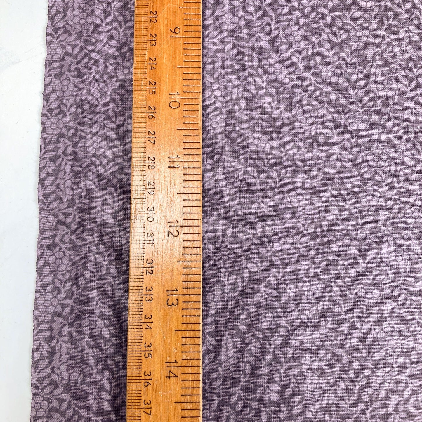 Purple cotton quiltback fabric with a small floral pattern with a wooden ruler for scale