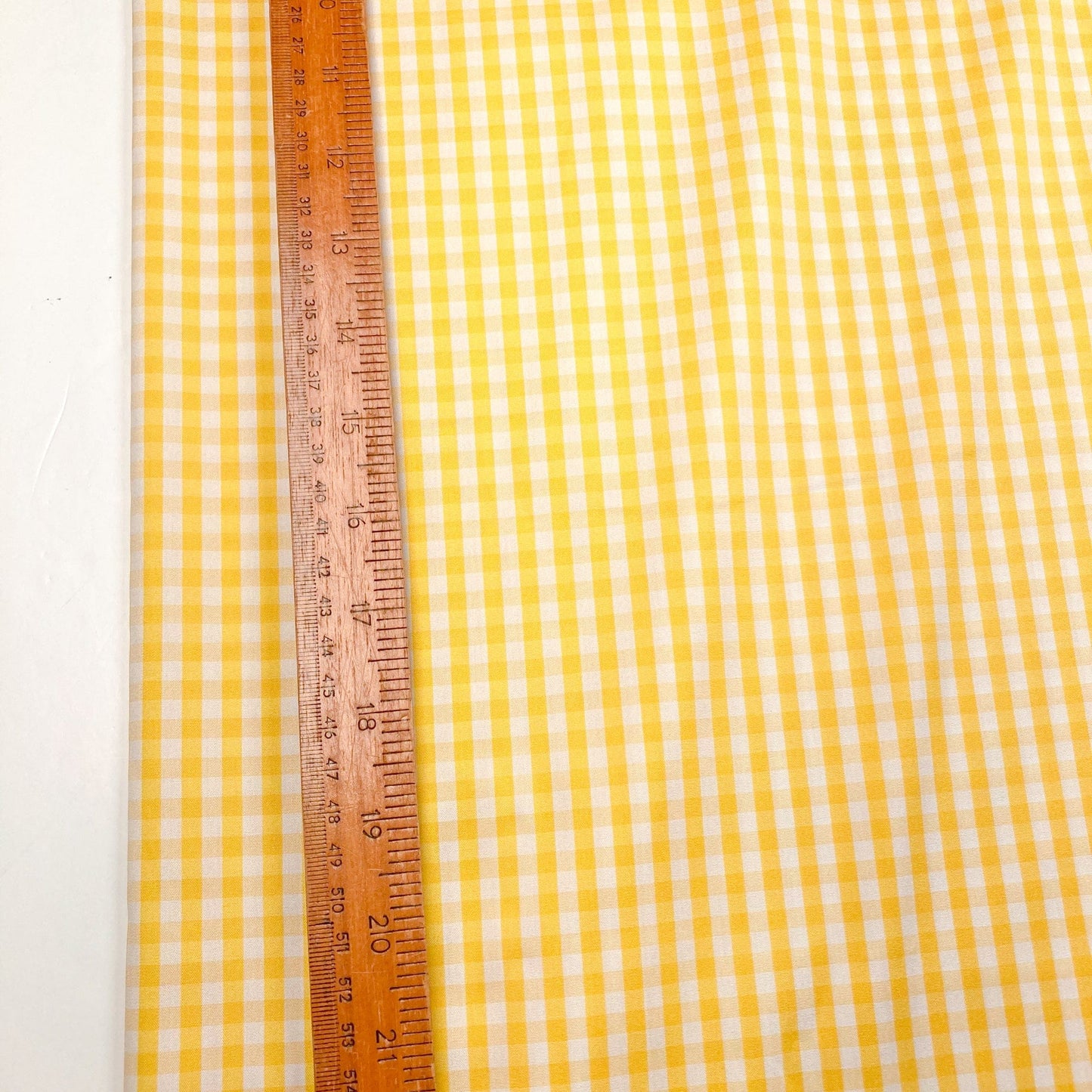 Yellow and white gingham fabric with a wooden ruler for scale on a white background