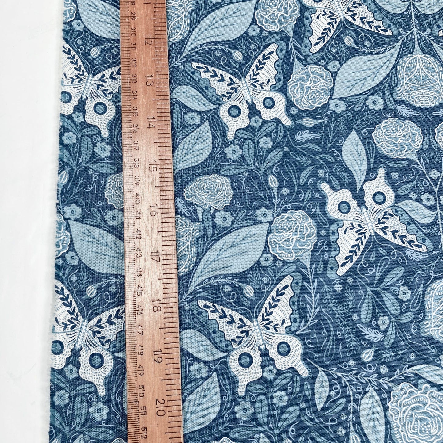Fabric with butterfly and floral pattern on a blue background, ruler for scale