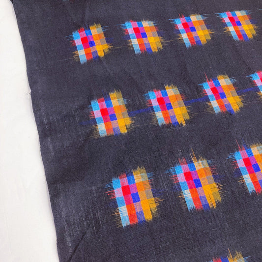 A lemgth of Indian handwoven ikat fabric with a deep black background and vibrant geometric check designs in multiple colors.