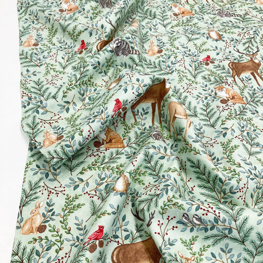 Quilting cotton with a nature-themed pattern featuring animals and plants on a light green background.