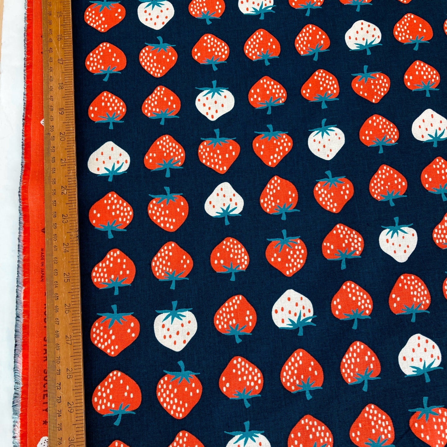 Fabric with strawberry pattern on a blue background, ruler for scale