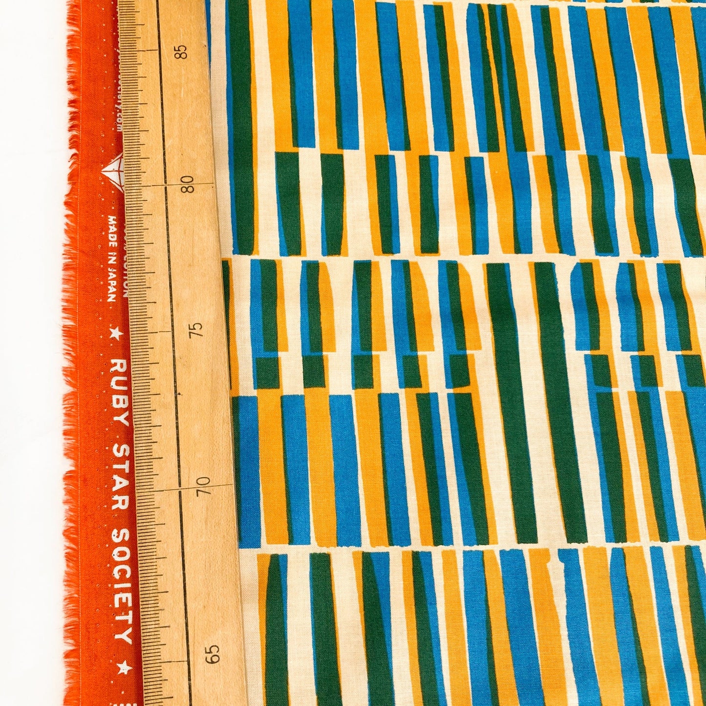 Colorful quilting cotton with a midcentury modern style geometric design in mustard, green and blue on a cream background. next to a ruler for scale