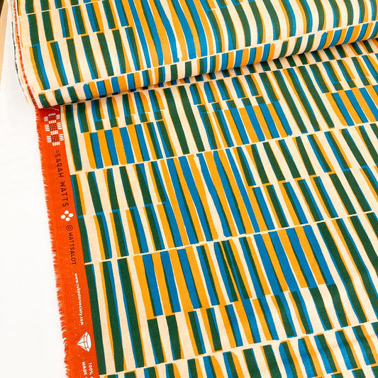 Bolt of colourful quilting cotton with a midcentury modern style geometric design in mustard, green and blue on a cream background.