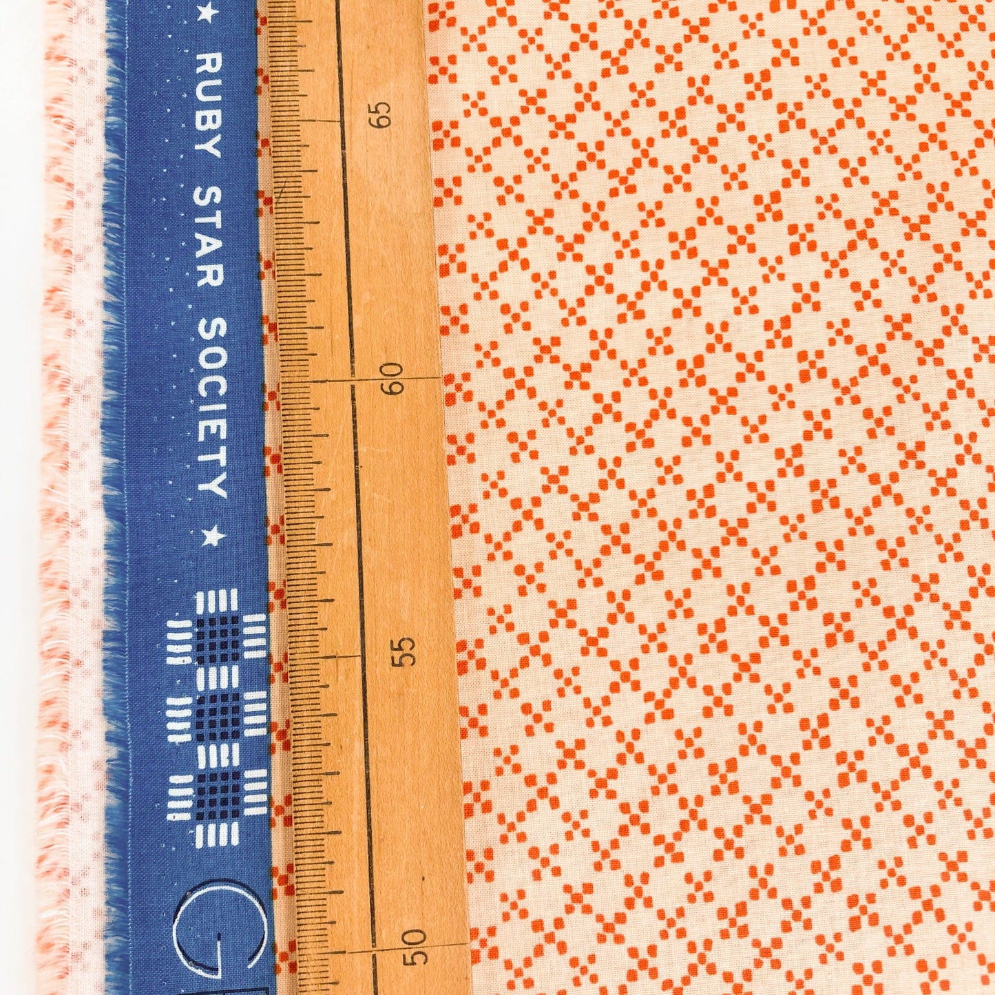 Quilting cotton fabric with an all-over tile print in terracotta on a cream background next to a ruler and Ruby Star Society selvedge.