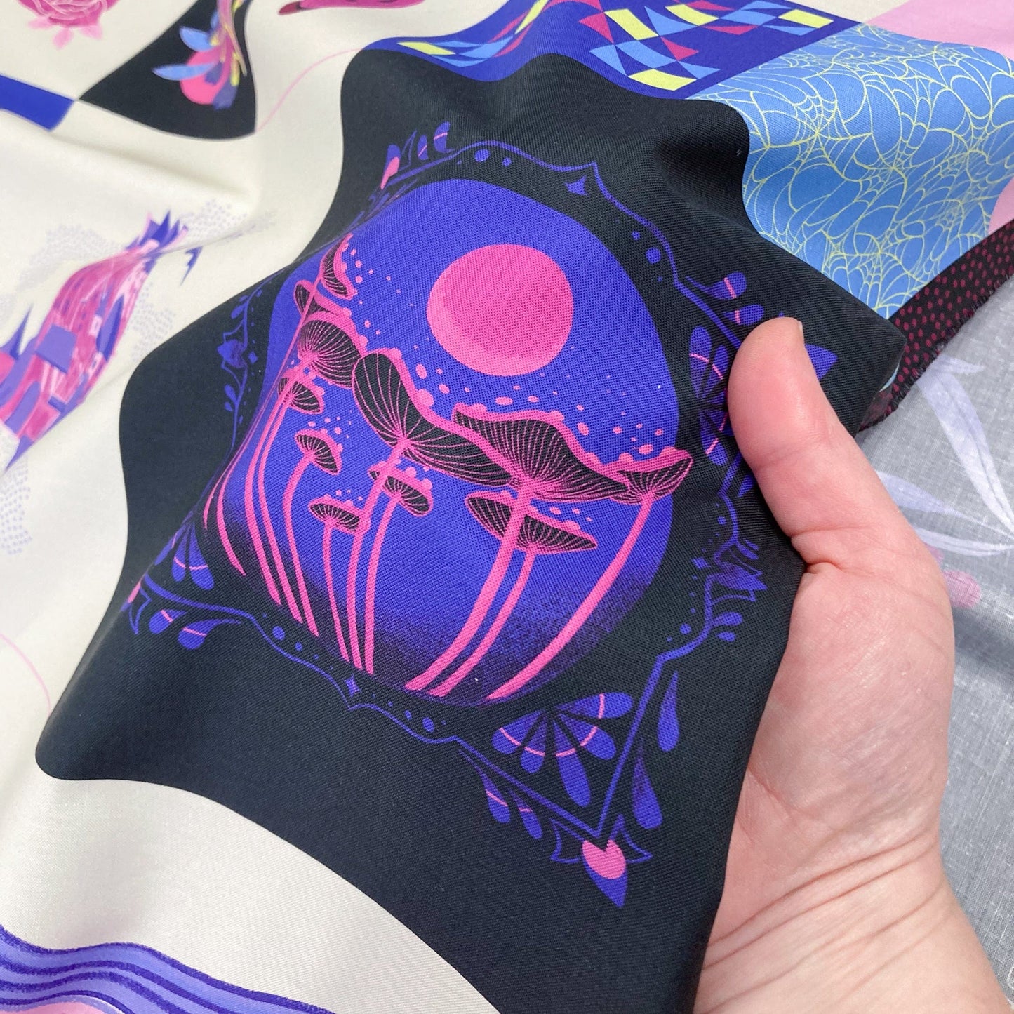 Hand holding a black fabric square element from a quilting cotton panel with pink and purple mushroom design.