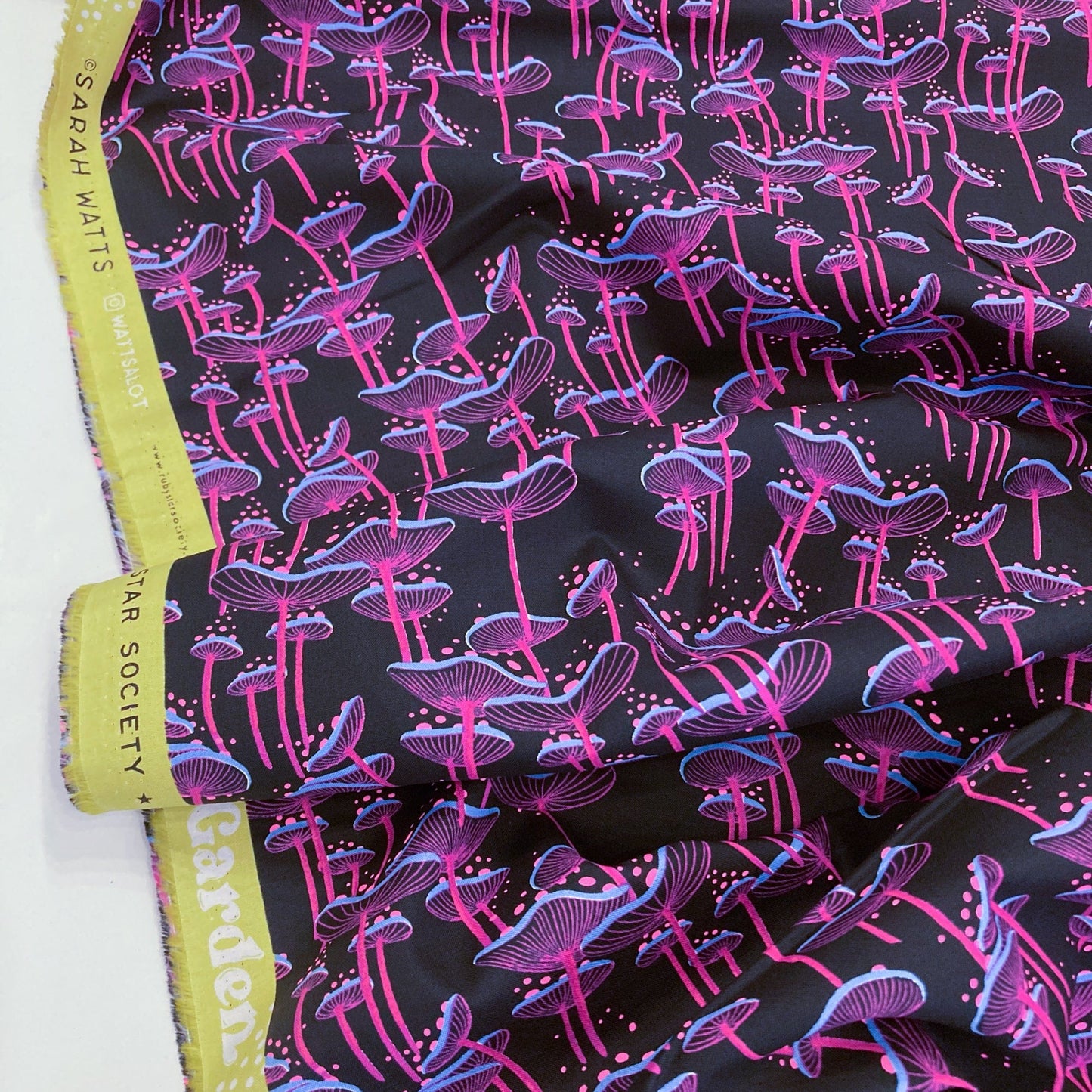 Fabric with neon pink and blue mushroom pattern on a black background.