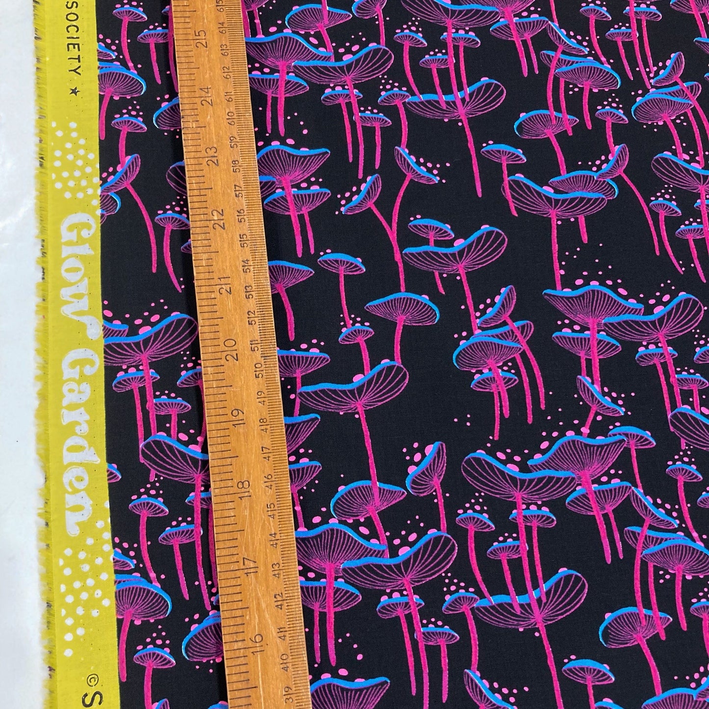 Patterned fabric with pink and blue mushrooms on a black background, measured by a ruler.