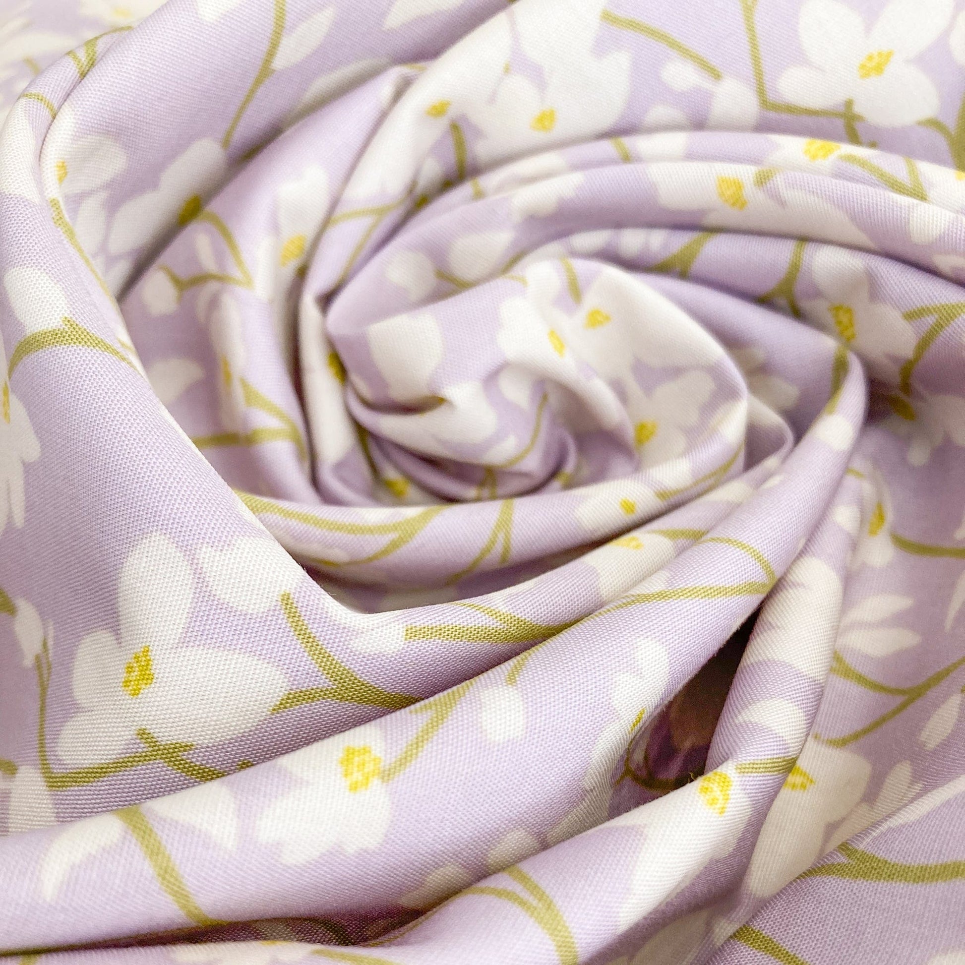 Swirl of floral cotton fabric with cream flowers on a lilac background.
