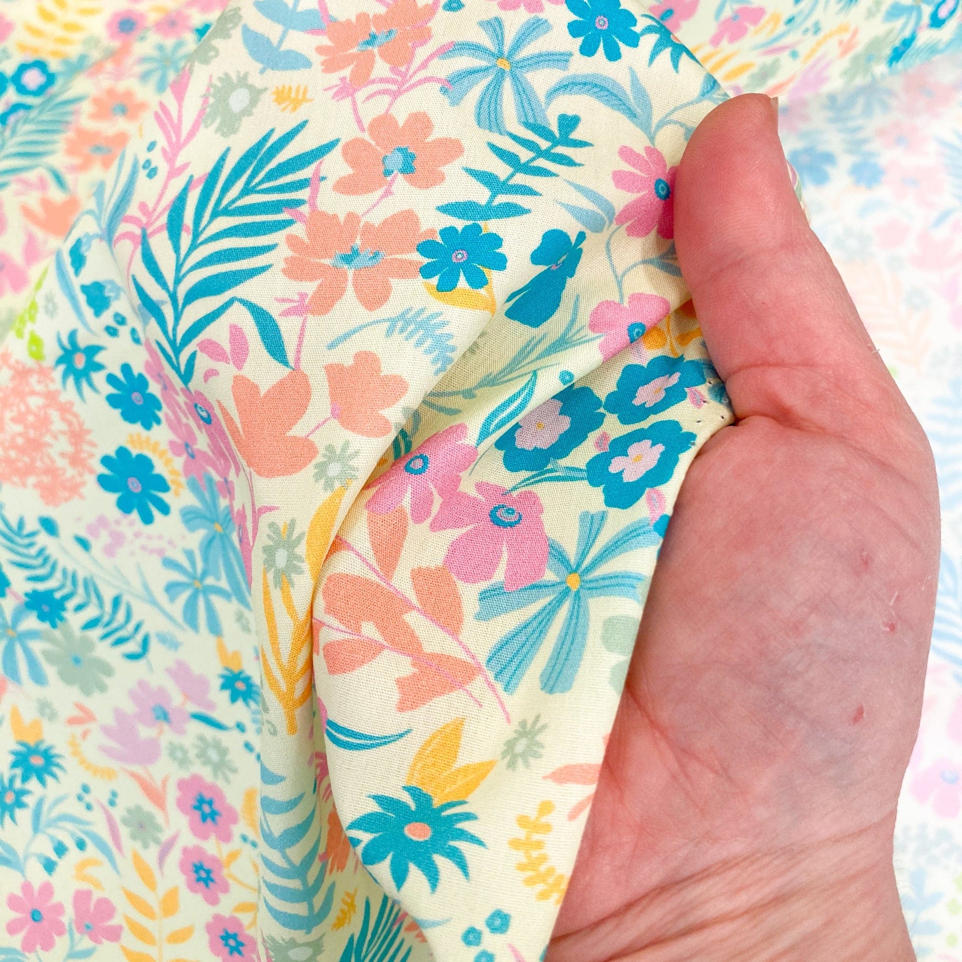 Hand holding floral quilting cotton by Art Gallery Fabrics with pink, blue, green, and yellow flowers on a yellow background