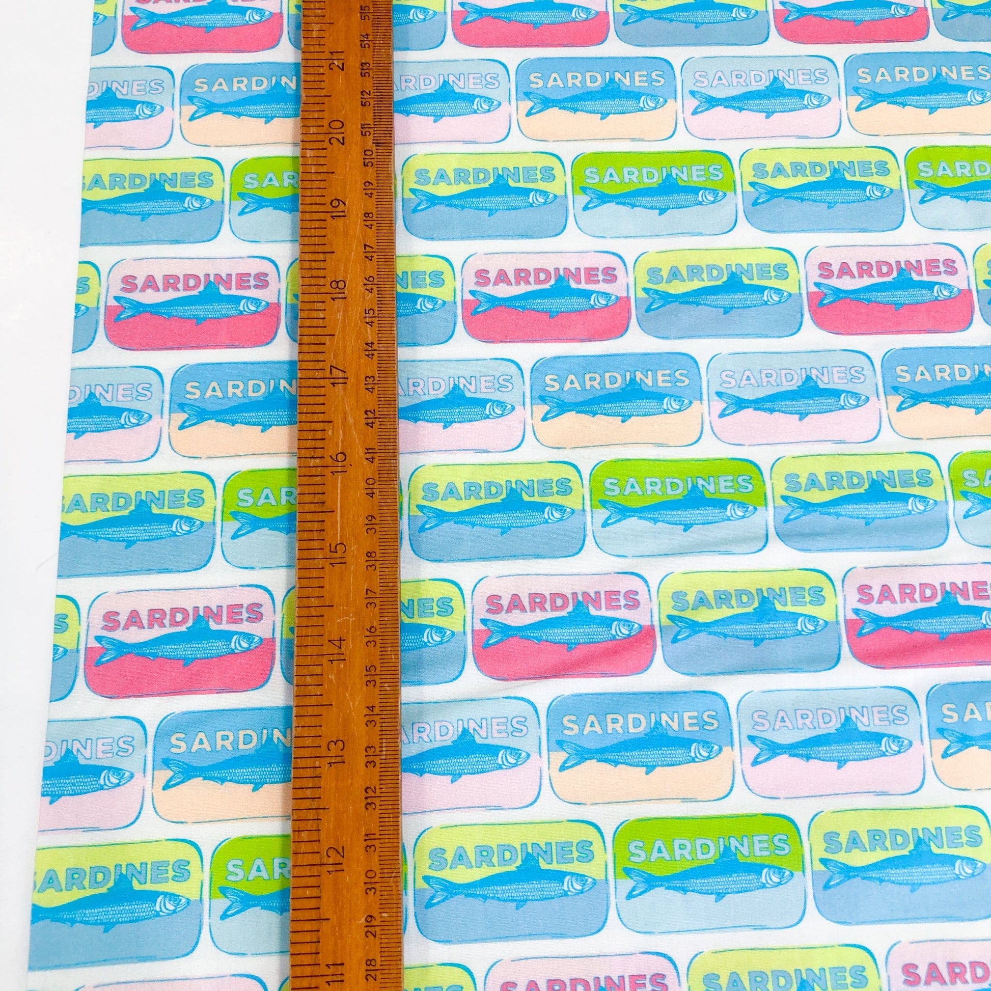 Quilting cotton with colorful pop-art style sardine tin pattern with a ruler for scale.