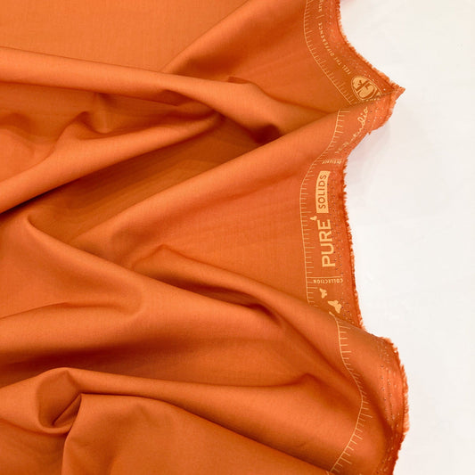 Close-up of burnt orange fabric with 'PURE SOLIDS Art Gellery Fabrics branding.