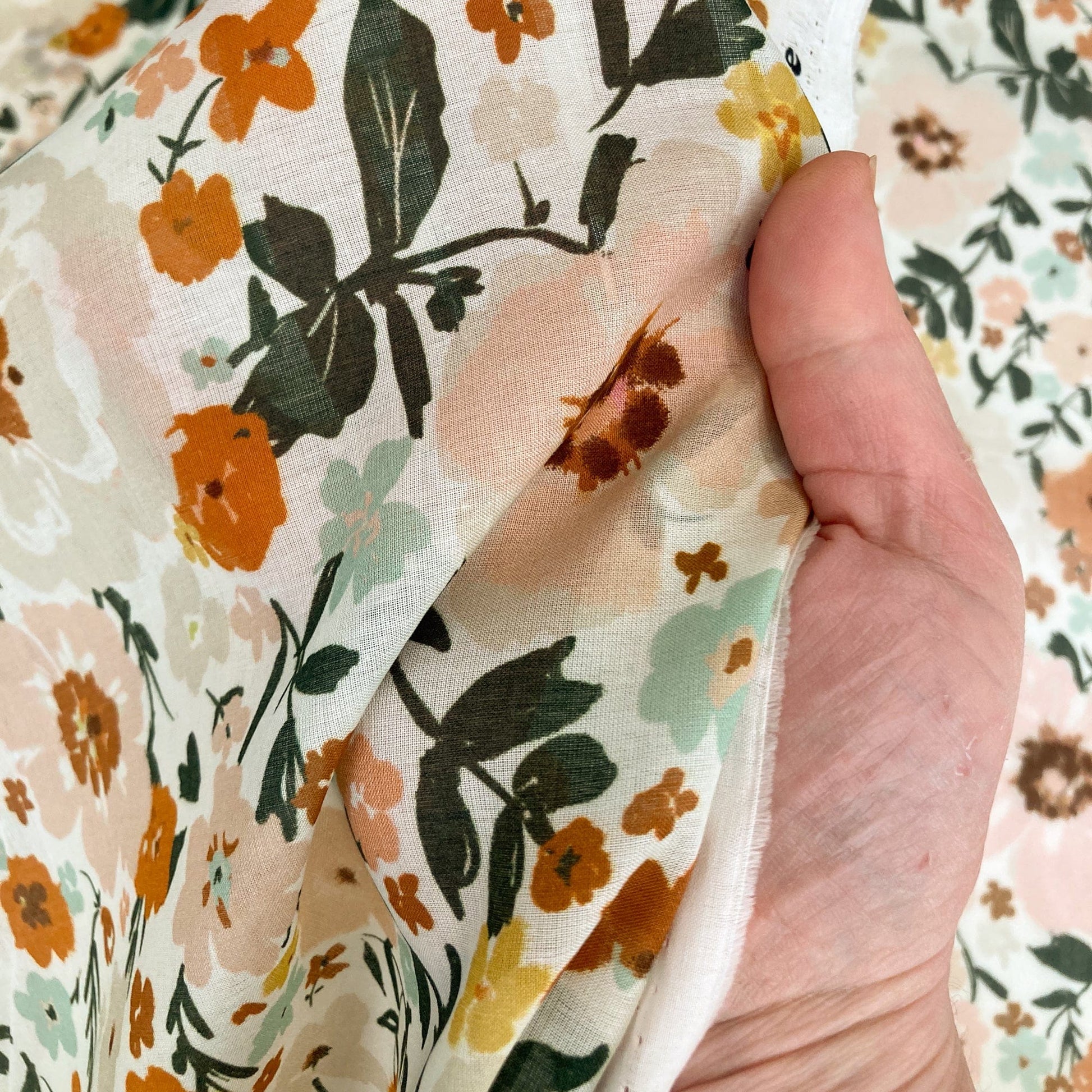 Hand holding floral batiste with a pattern of flowers and leaves.