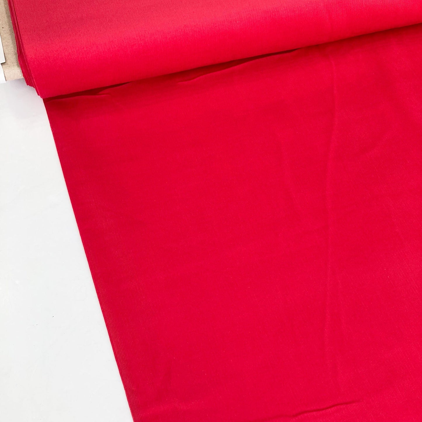 Bolt of red needlecord fabric on a white background