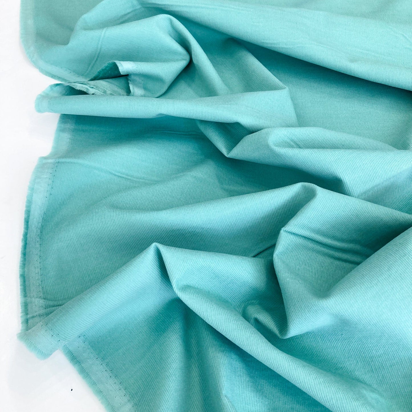 Close-up of turquoise cotton needlecord fabric against a white background