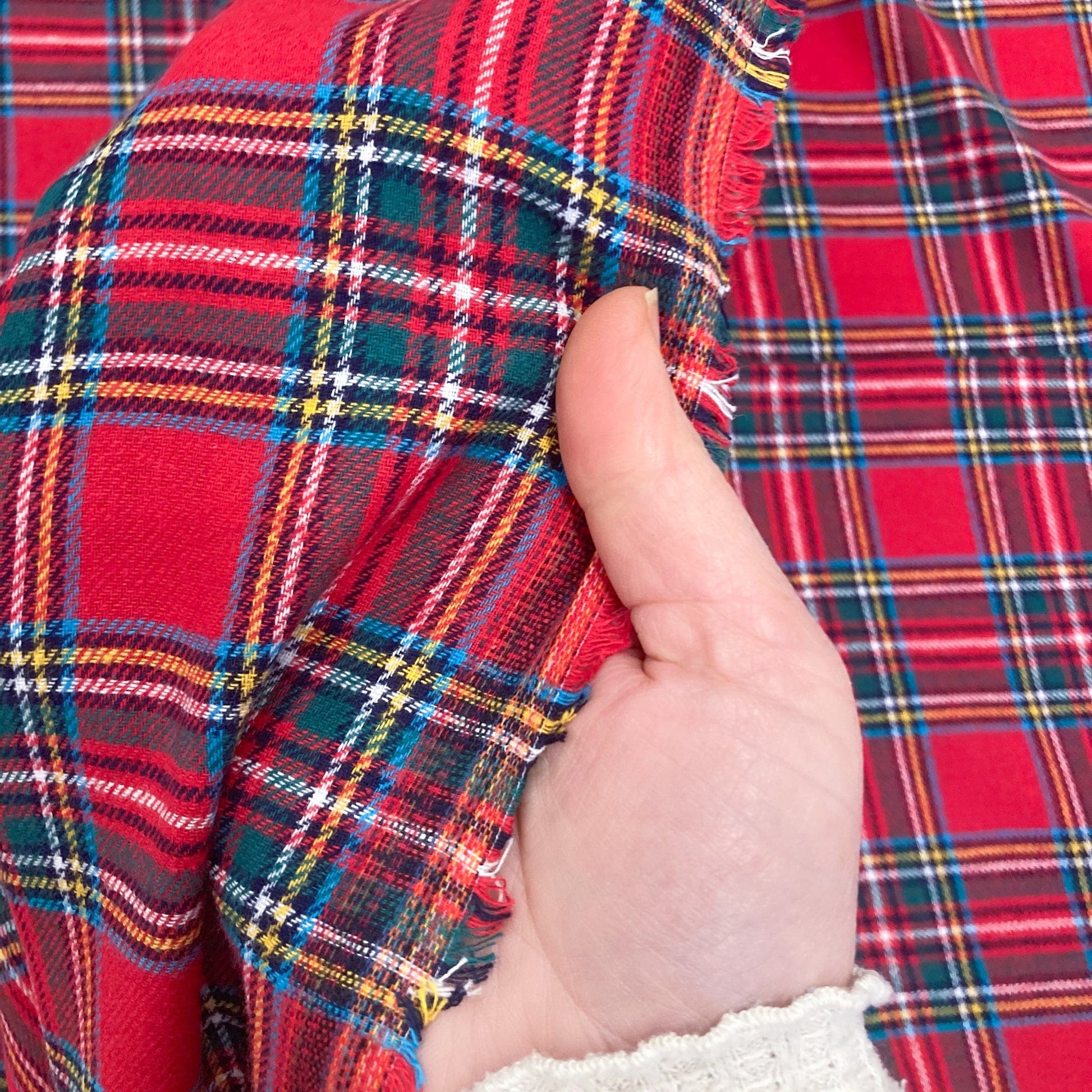 Hand holding red tartan brushed cotton fabric with a close-up view