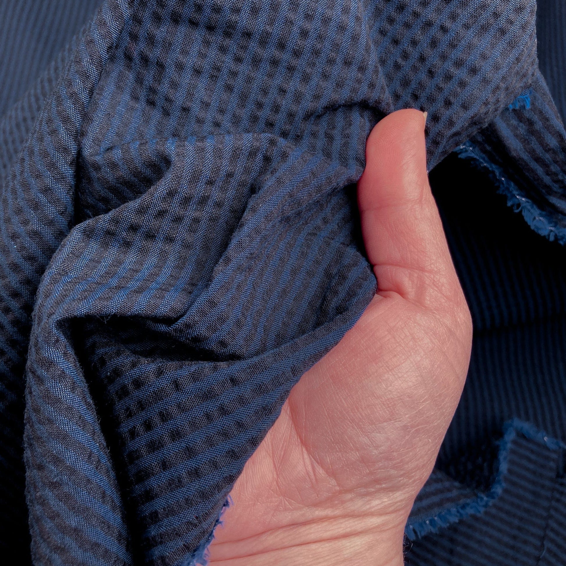 Hand holding blue striped cotton seersucker fabric