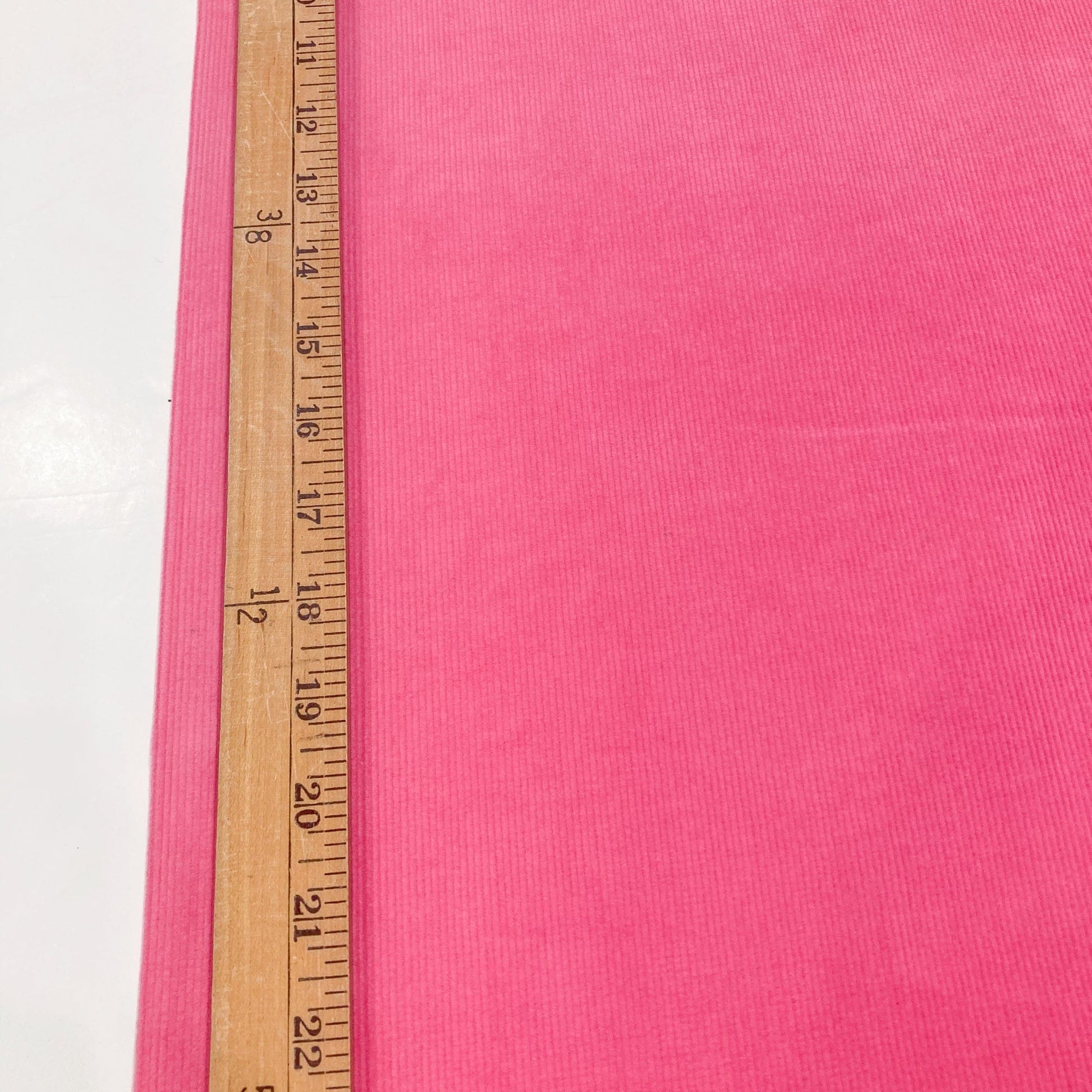Bright pink cotton corduroy fabricwith a wooden measuring ruler for scale