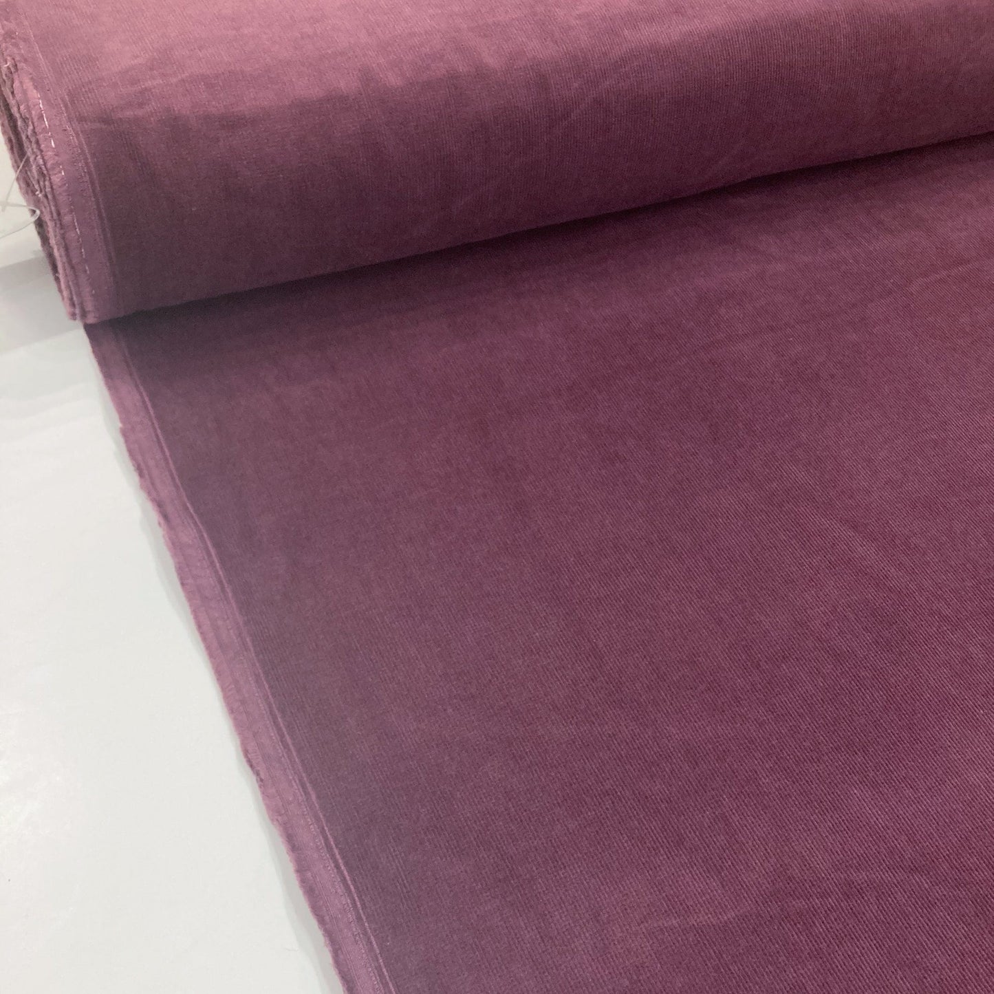 Bolt of purple cotton corduroy fabric on a white background