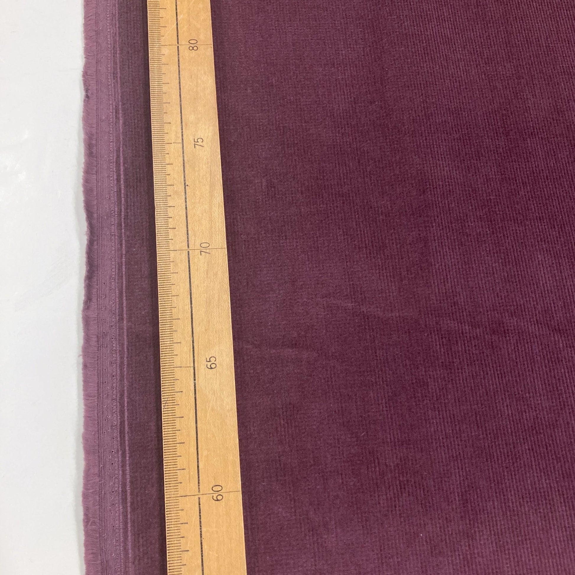 Purple corduroy fabric with a wooden ruler for scale on a white background
