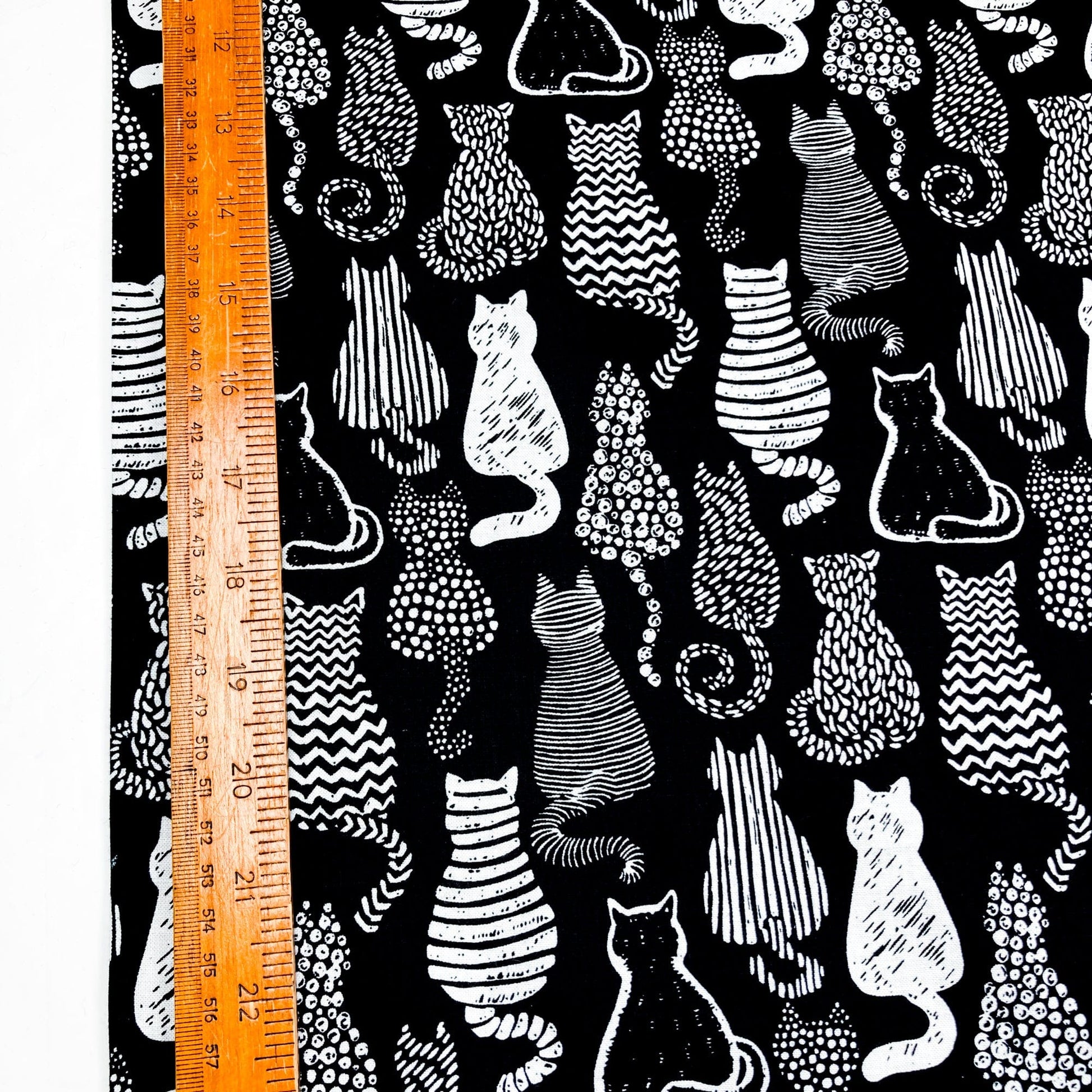 Cotton fabric with a graphic style cat print in black and white shown against a ruler for scale.