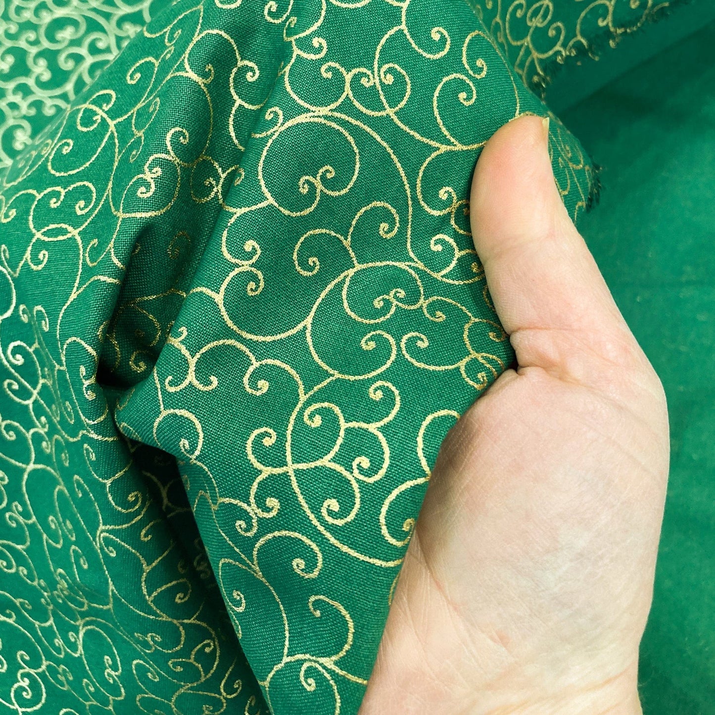 Green quilting cotton with celtic style metallic gold swirl pattern held by a hand