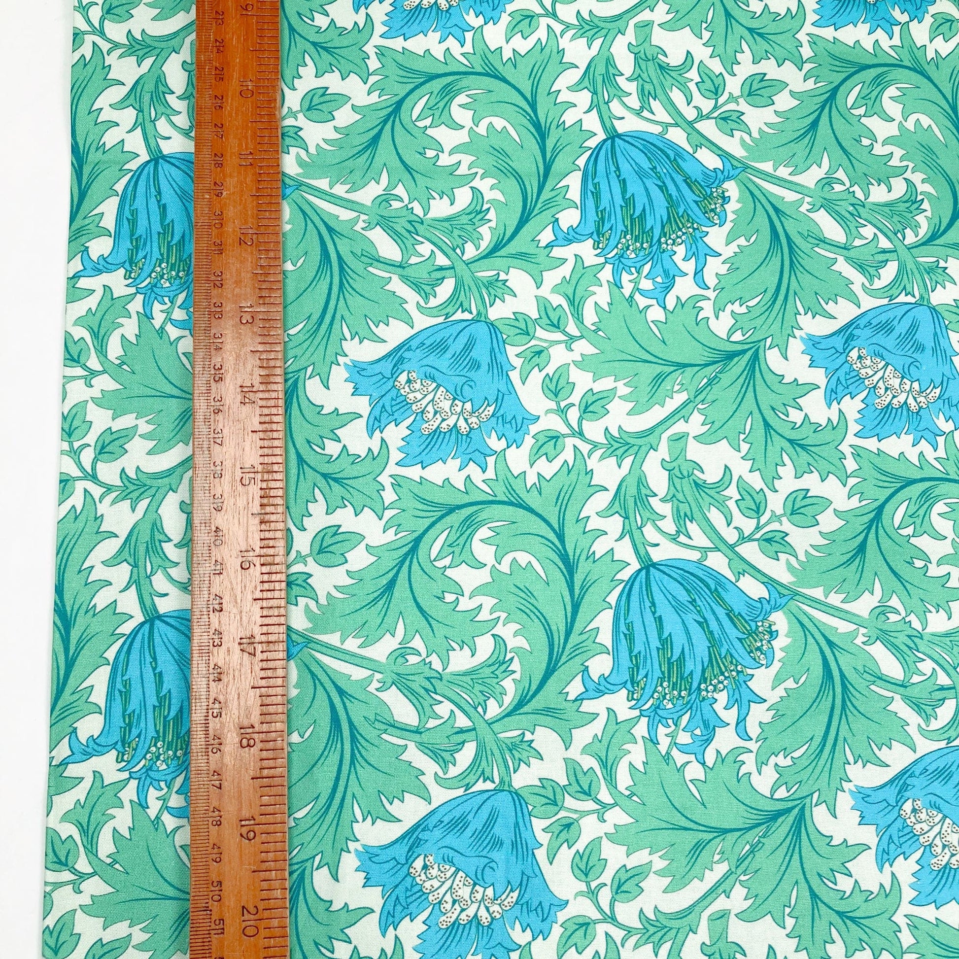 Cotton fabric with William Morris Style floral print in green and blue shown with a ruler for scale