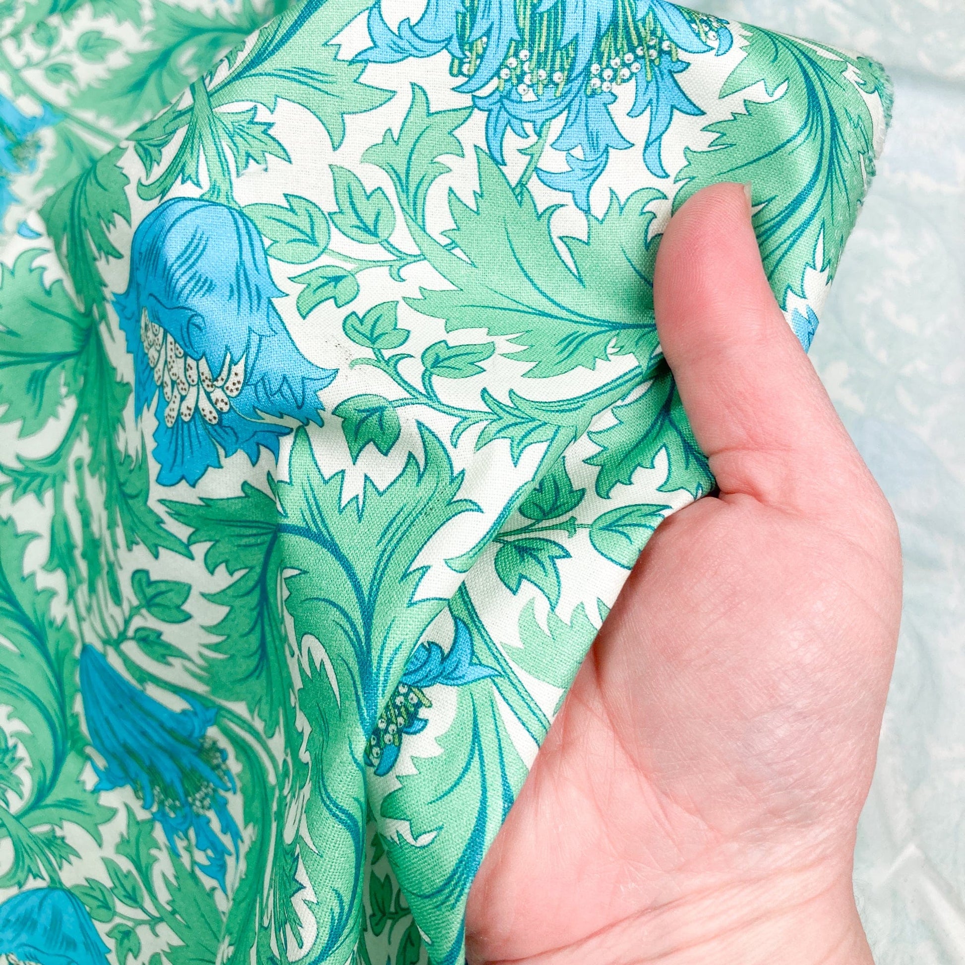 Cotton fabric with William Morris Style floral print in green and blue shown against a hand