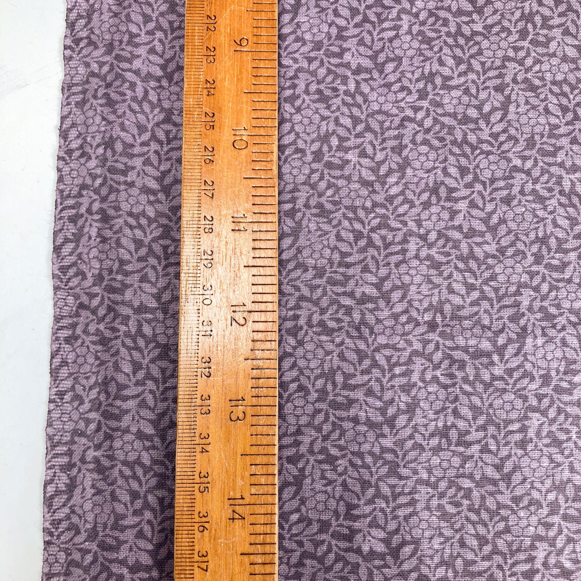 Purple cotton quiltback fabric with a small floral pattern with a wooden ruler for scale 