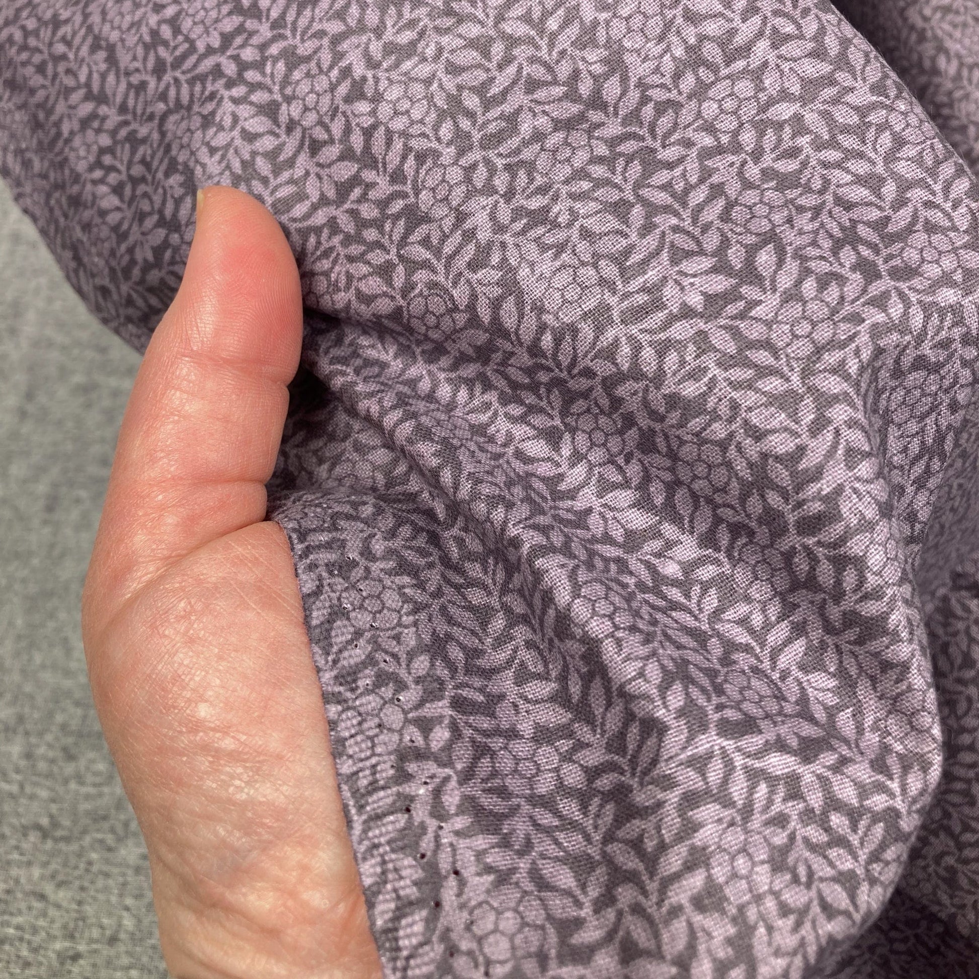 Close-up of a hand holding purple cotton quiltback fabric with a small floral pattern 