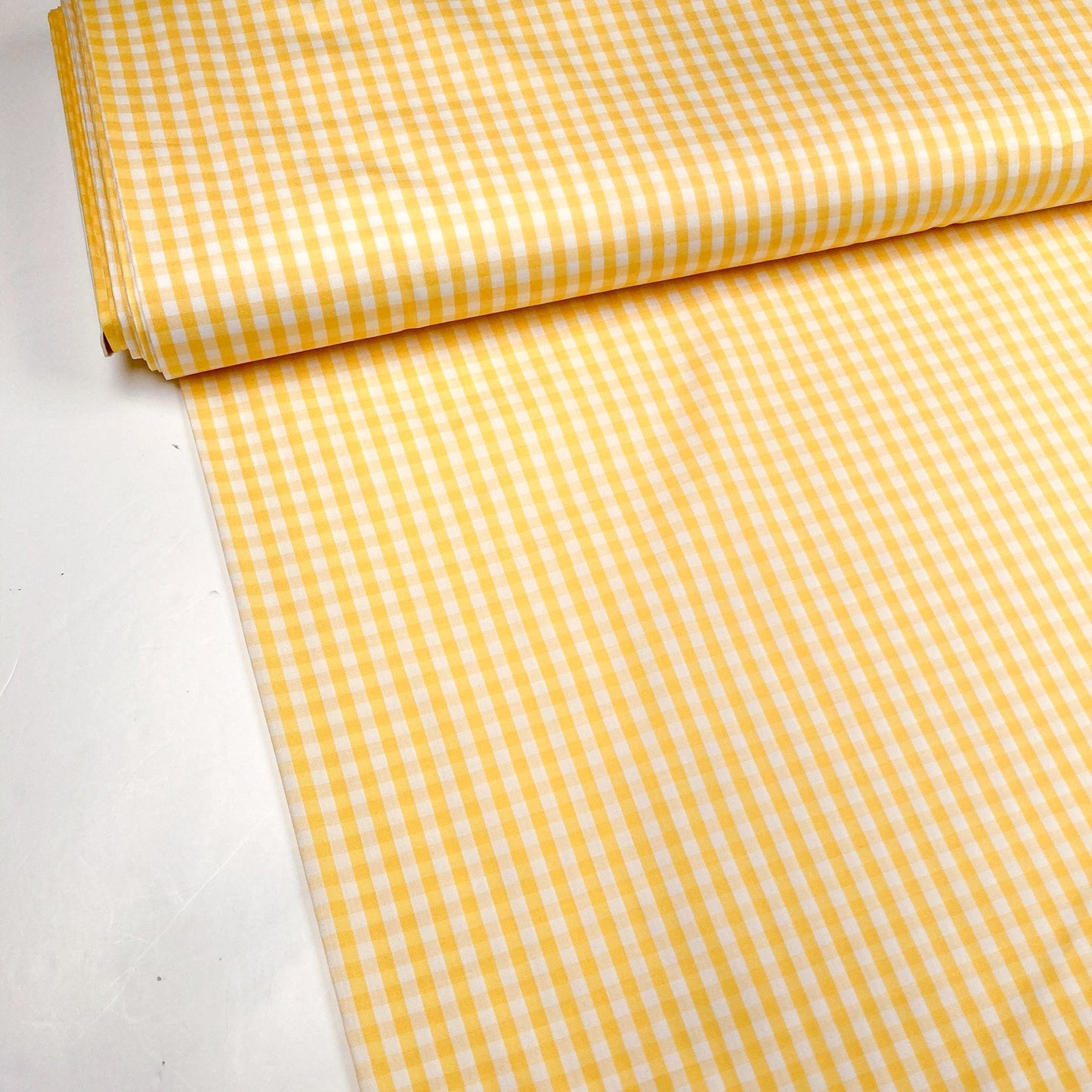A bolt of yellow and white gingham fabric against a white background
