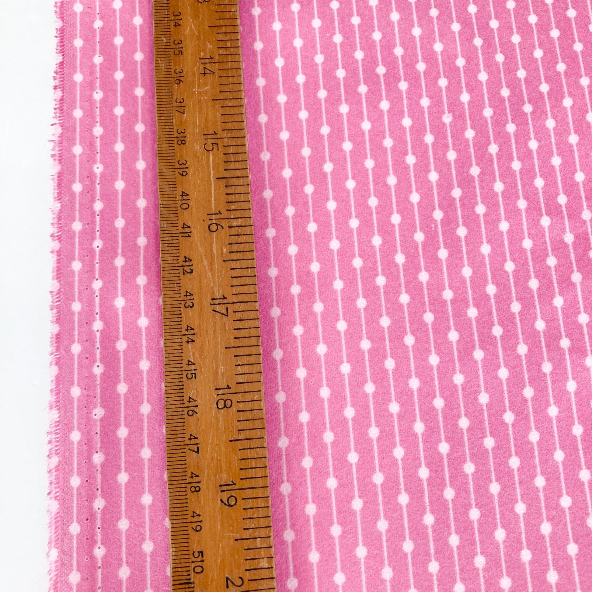 Pink fabric with white polka dots and a wooden ruler for scale.