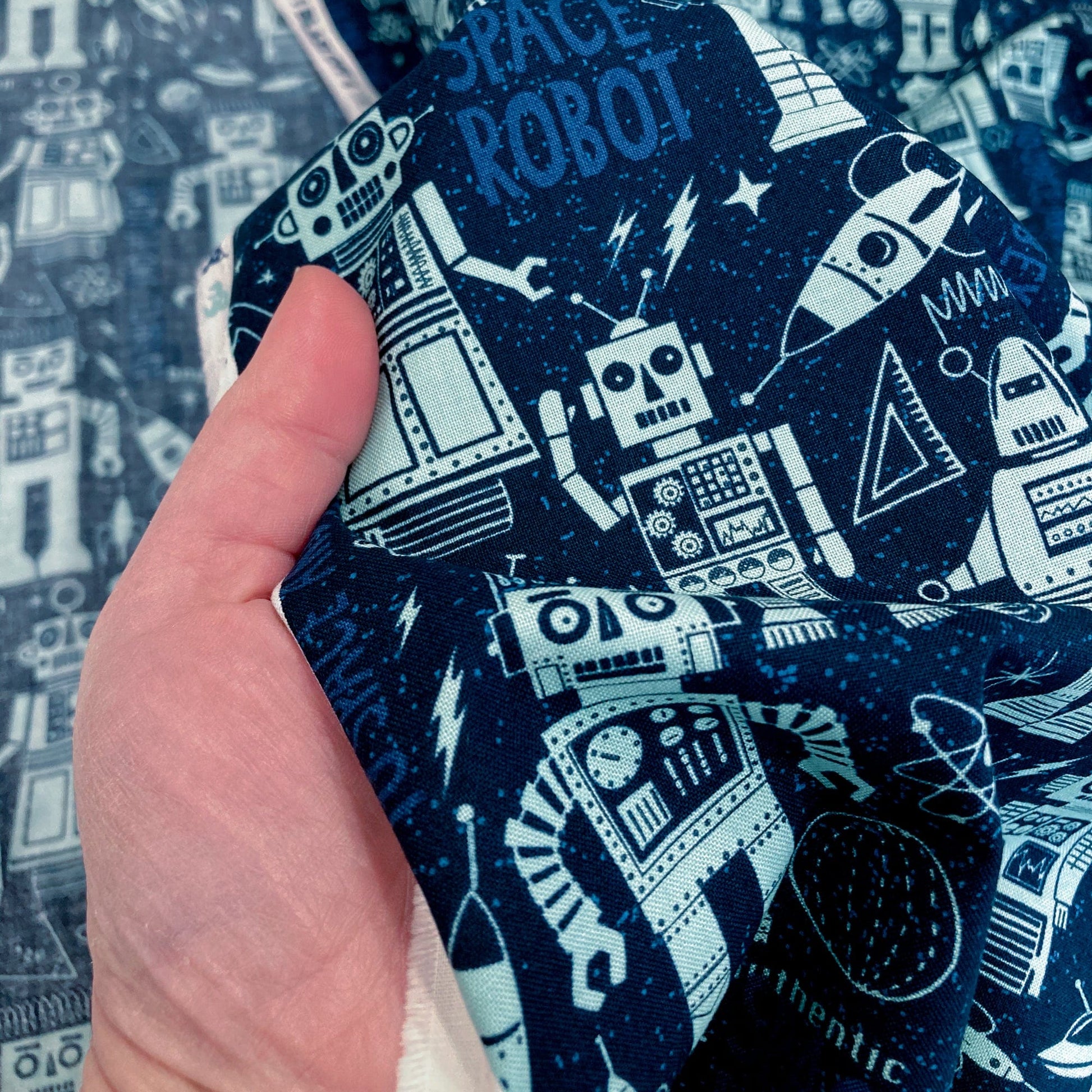 Hand holding quilting cotton fabric with robot pattern in blue.
