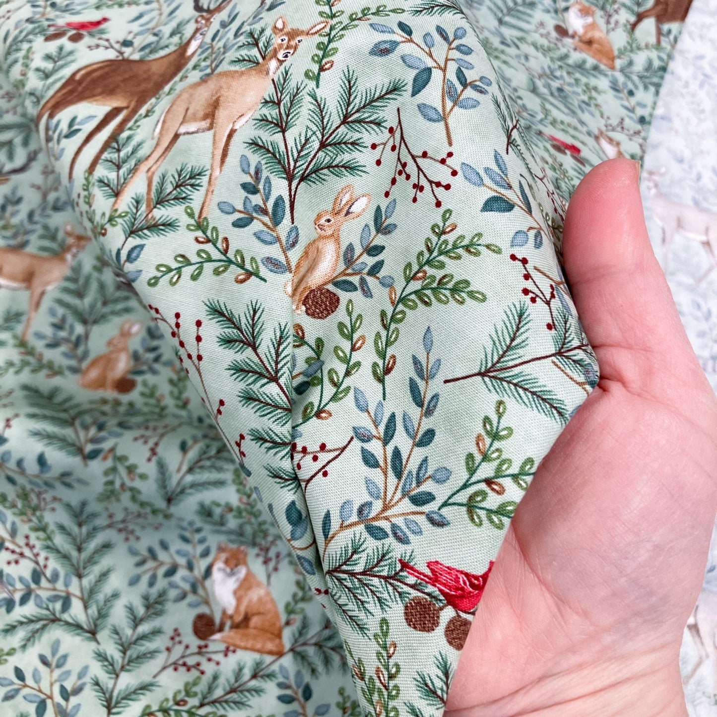 Hand holding cotton fabric with a nature-themed pattern featuring animals and plants.