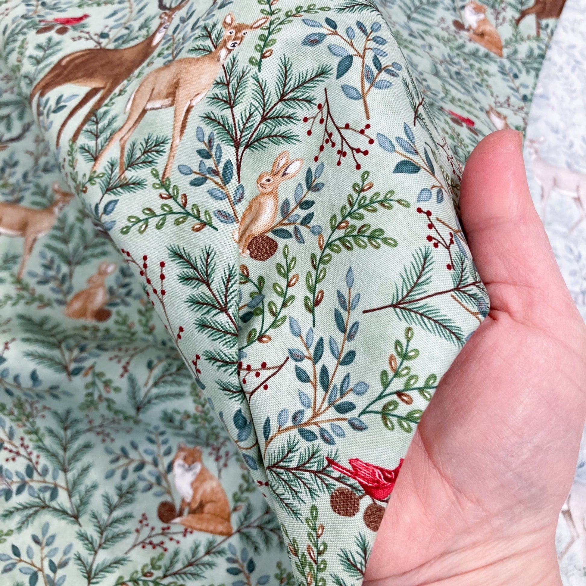 Hand holding cotton fabric with a nature-themed pattern featuring animals and plants.