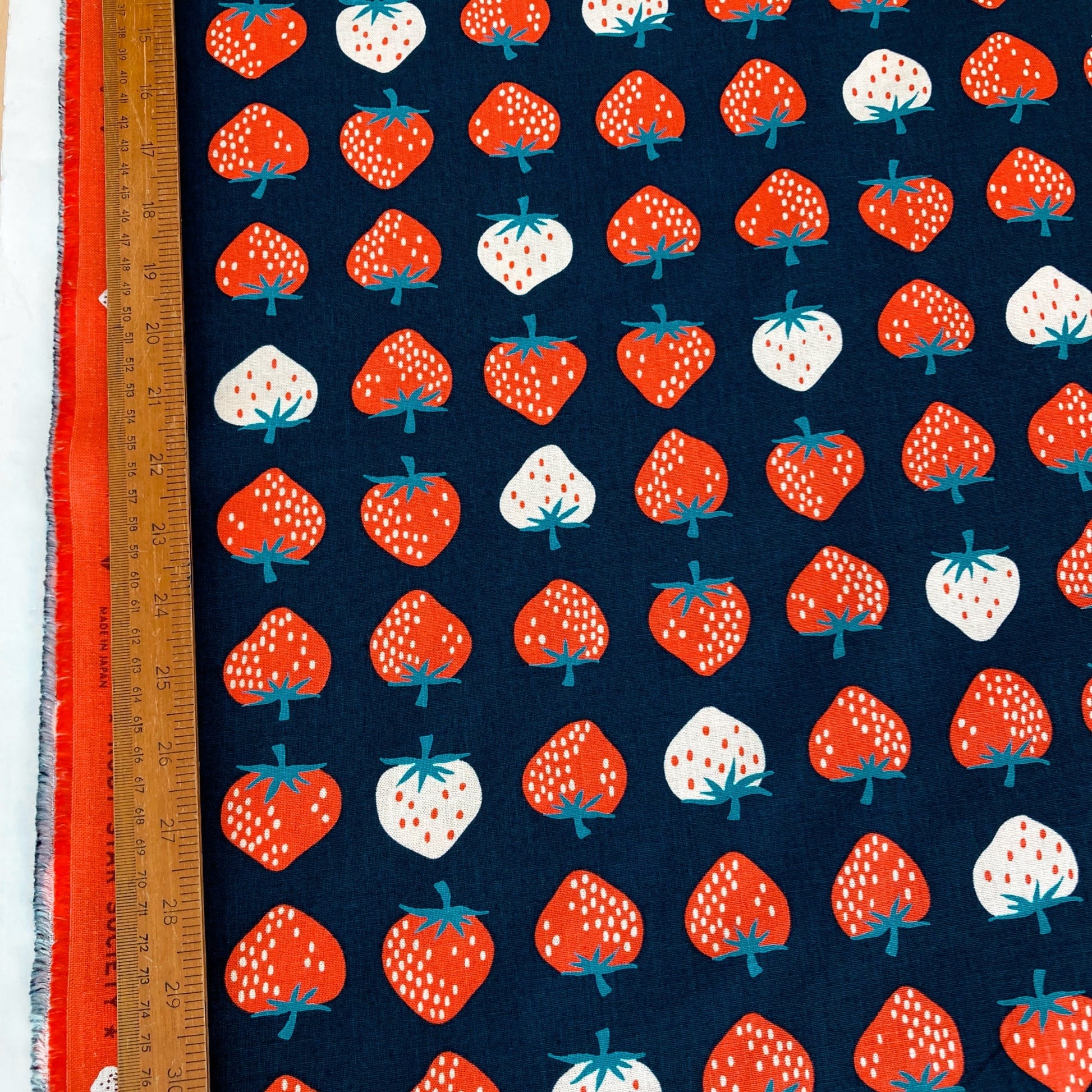 Fabric with strawberry pattern on a blue background, ruler for scale